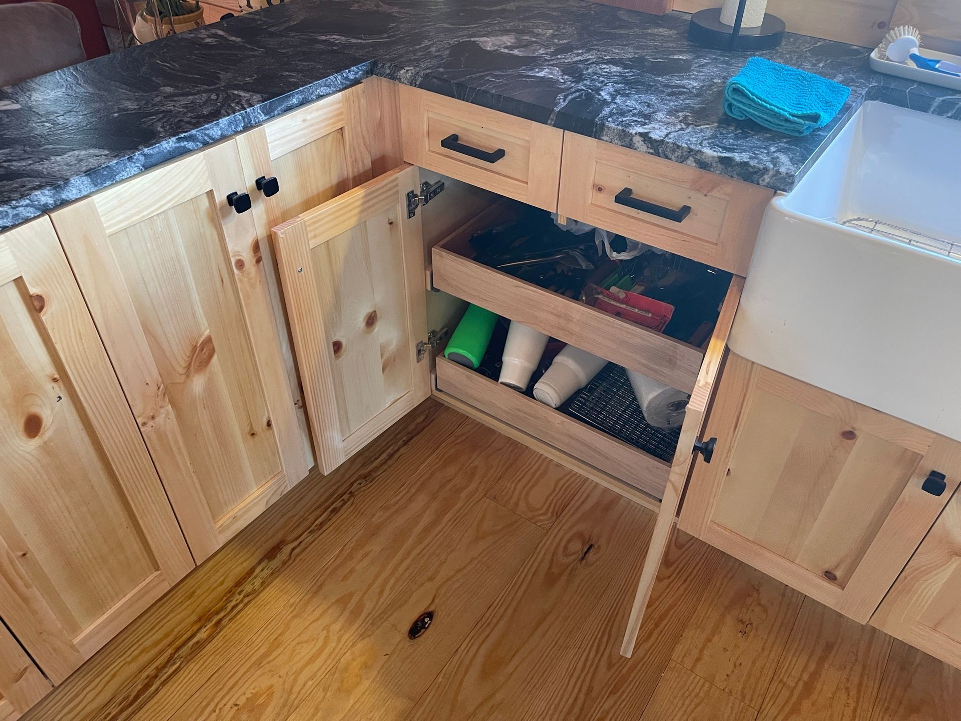 Wooden kitchen cabinets with a pull-out shelf. Open door reveals cleaning supplies.