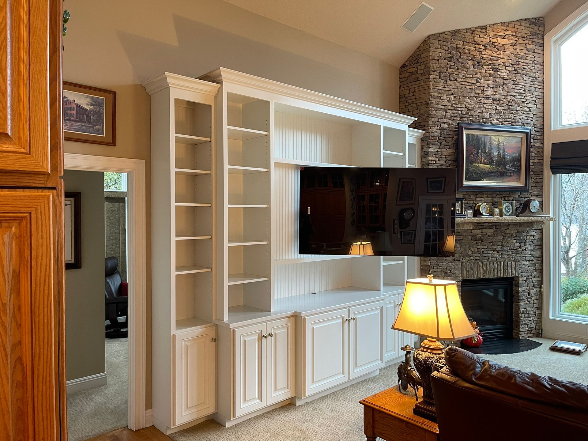 Built-in white media center with TV, storage, and bookshelves in a living room; fireplace and window in background.