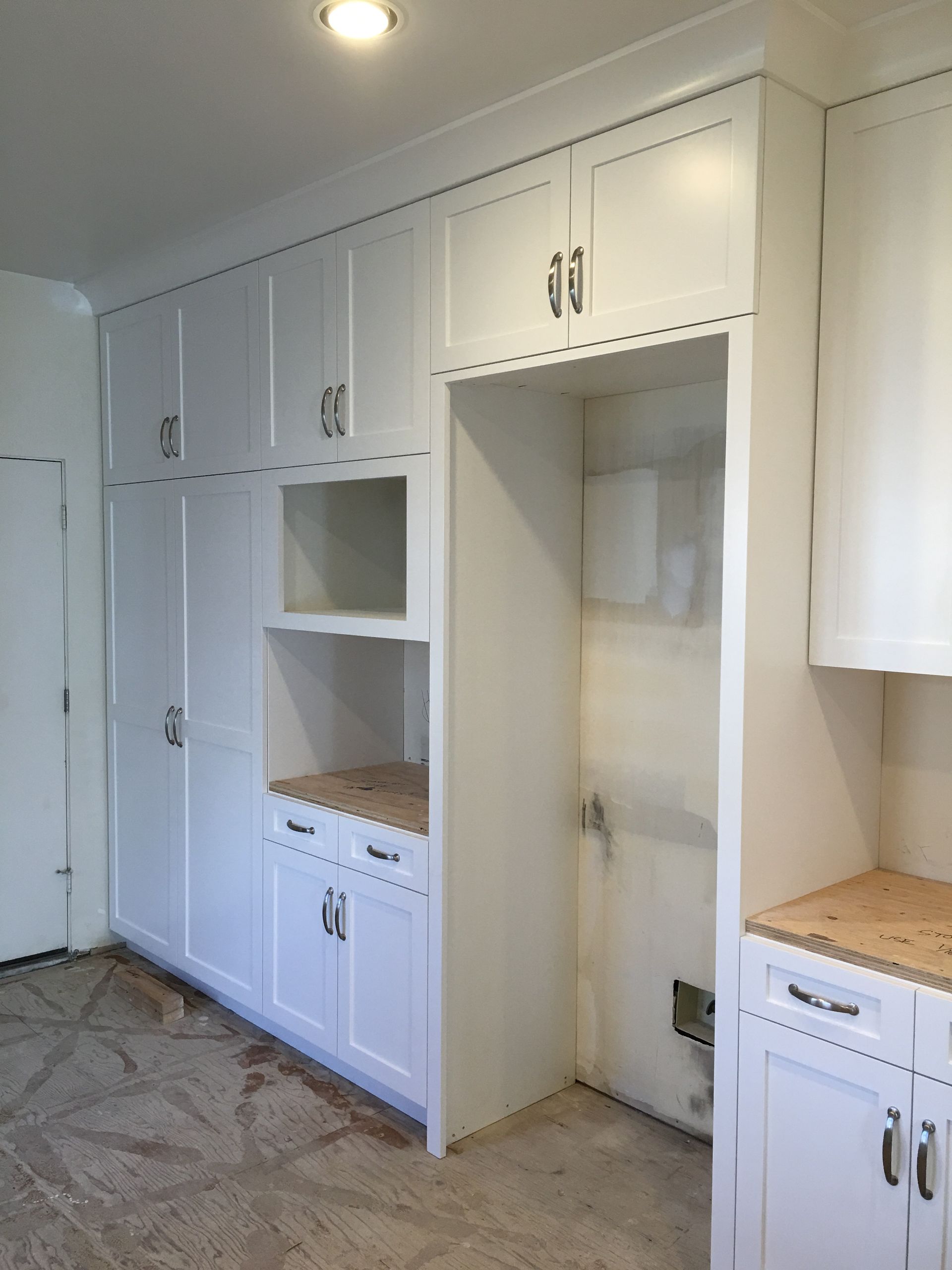 White kitchen cabinets with an open space for a refrigerator and a built-in oven.