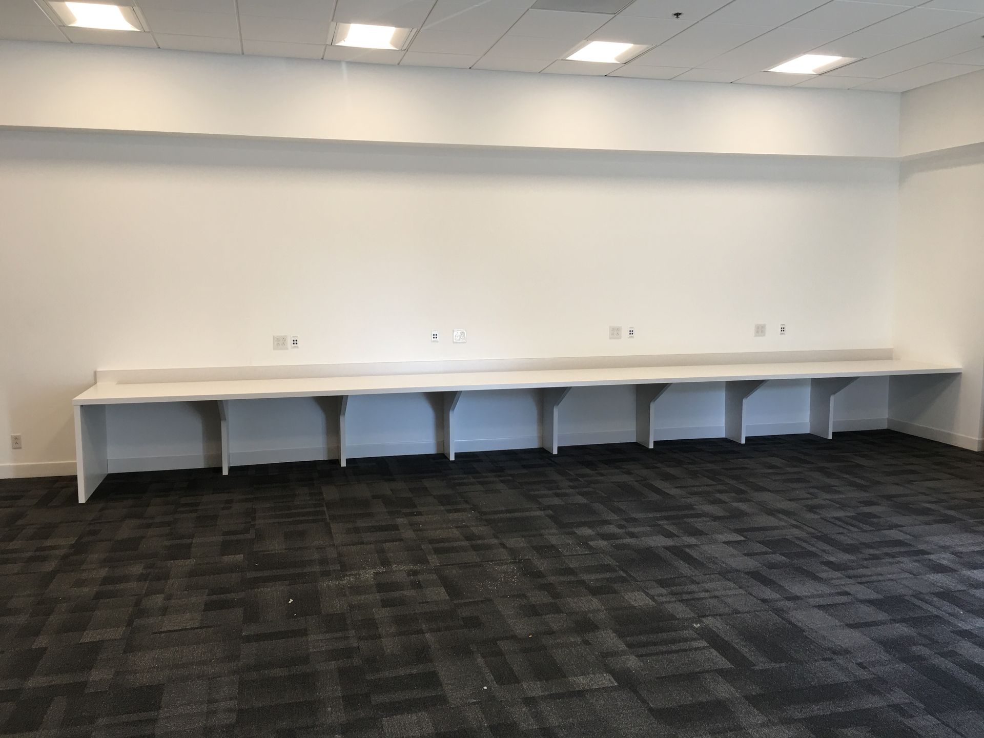 Empty room with long white desk against a white wall and dark carpet.