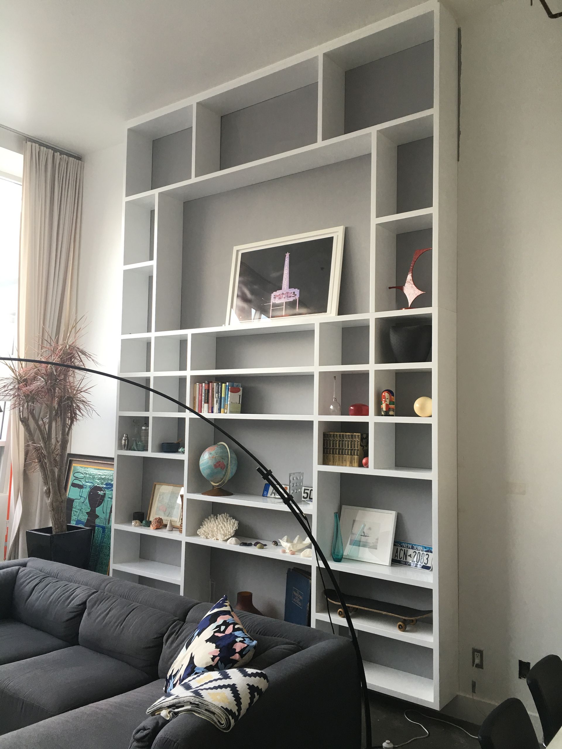 White built-in shelving unit filled with objects against a gray wall. A dark gray sofa sits below.