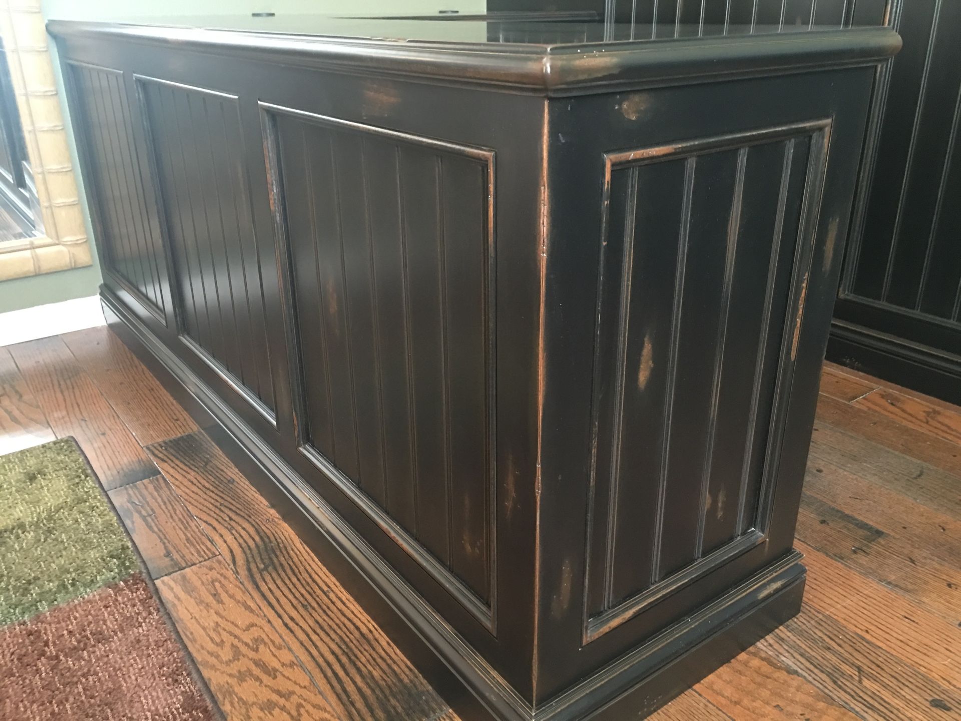 Black distressed wooden cabinet with vertical paneling, sitting on a wood floor.