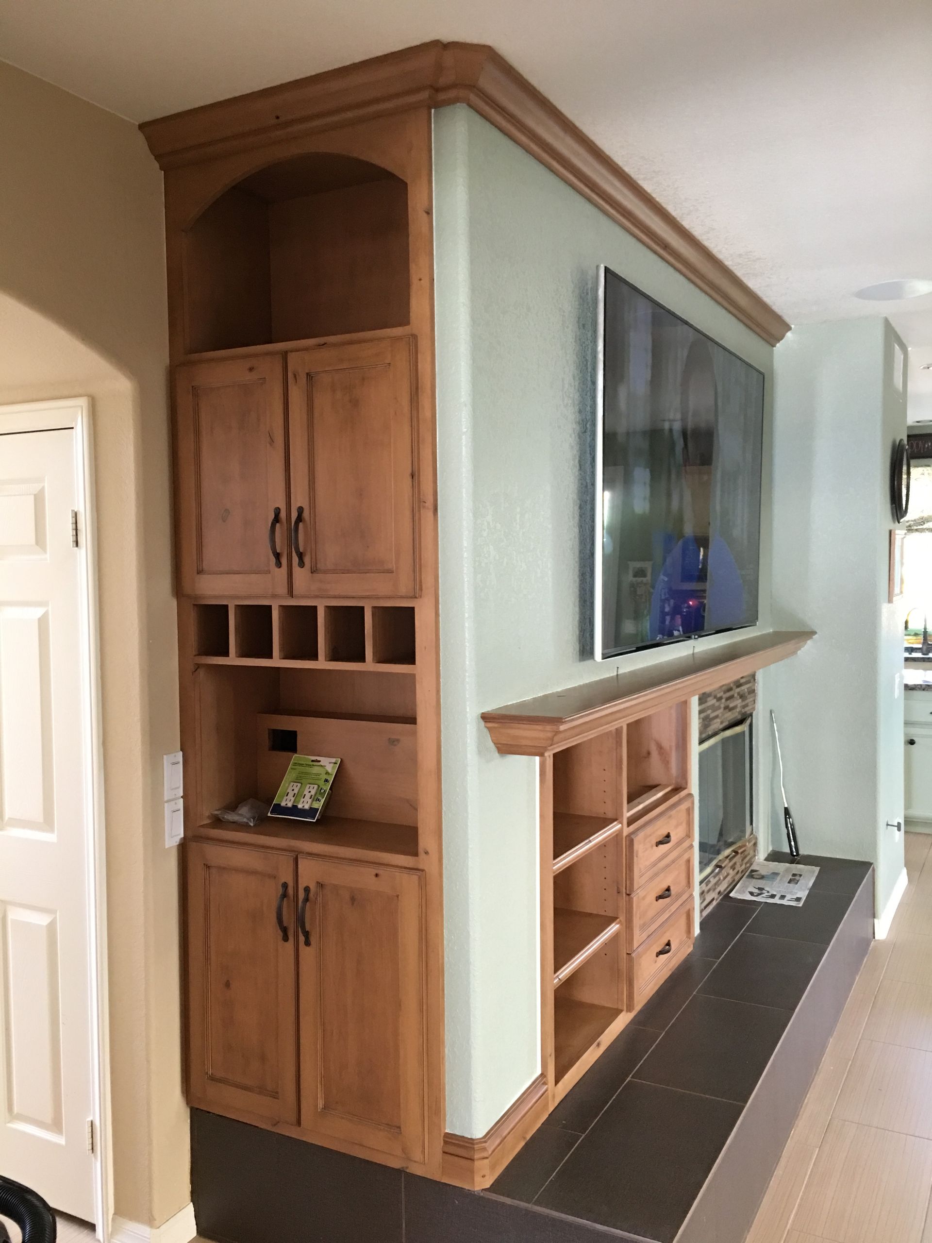 Built-in wooden cabinet with open shelves, cabinets, and a wine rack; a mounted TV above a fireplace.