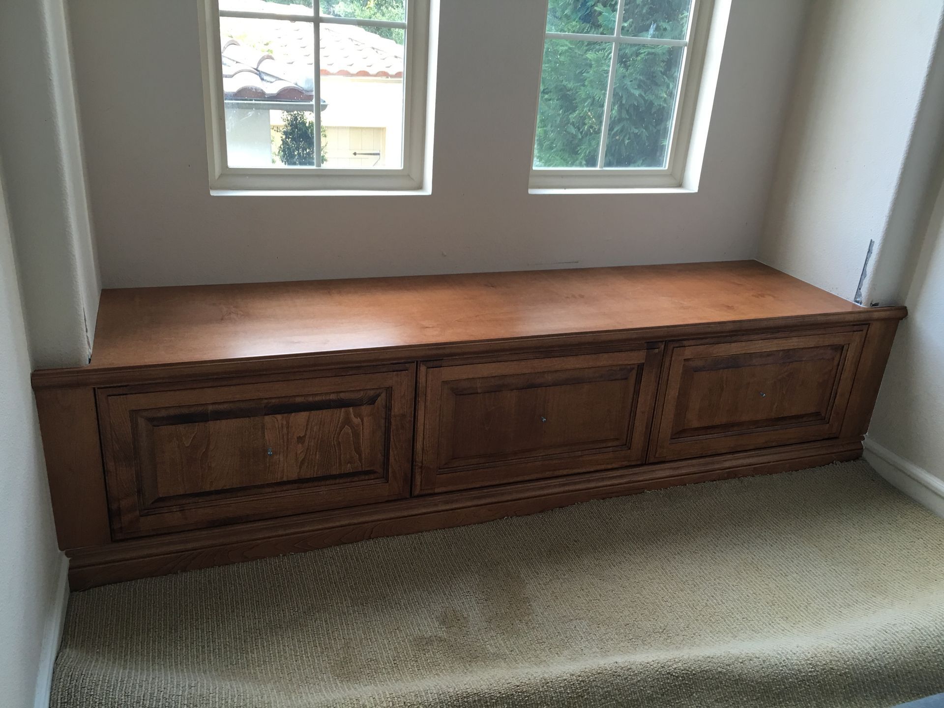 Wooden built-in bench with three panels, below two windows. Light-colored carpet.