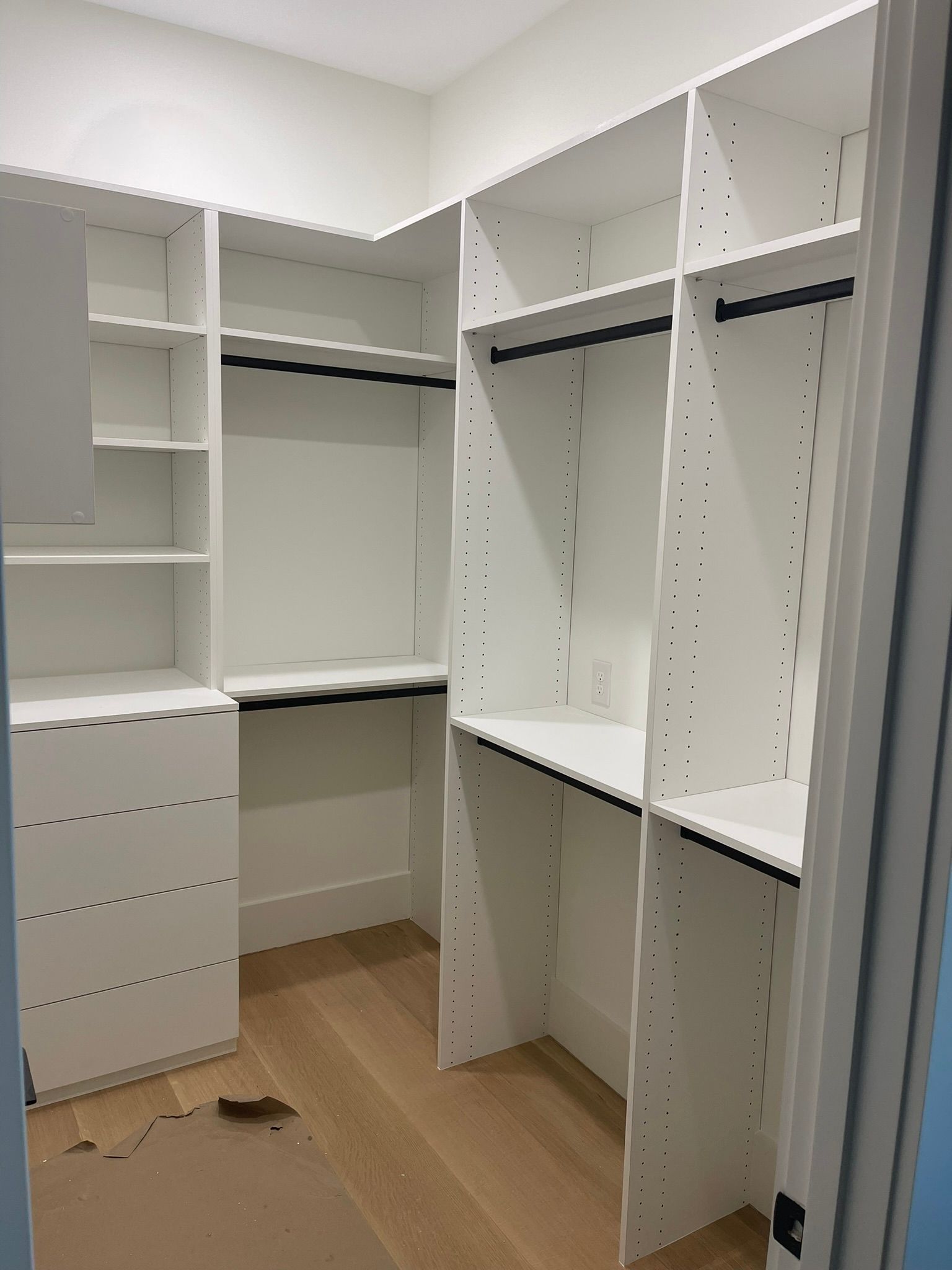 White walk-in closet with shelves and hanging rods. Light wood floor.