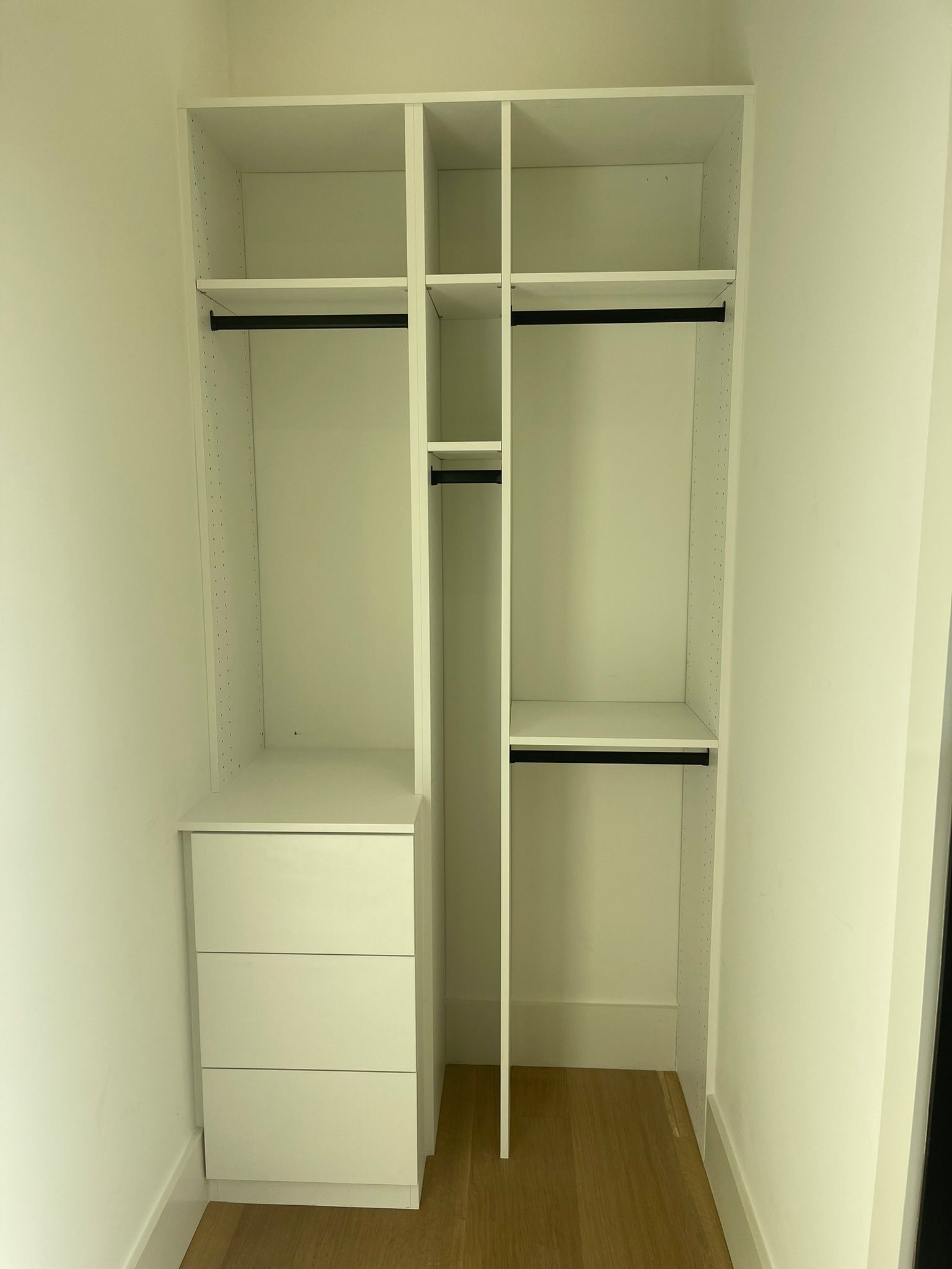 White closet organizer with drawers, shelves, and hanging rods.