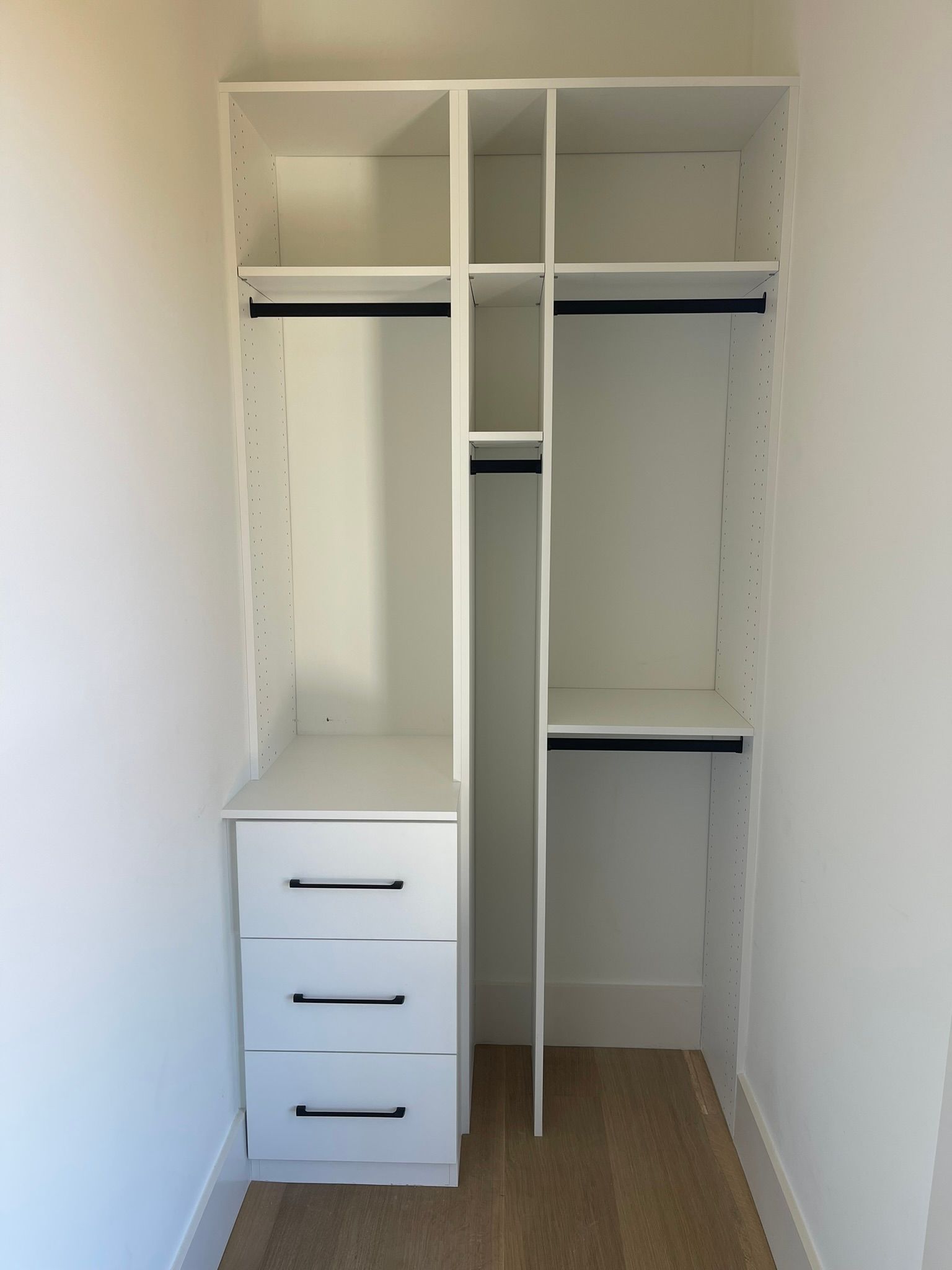 White closet shelving unit with drawers and hanging rods.