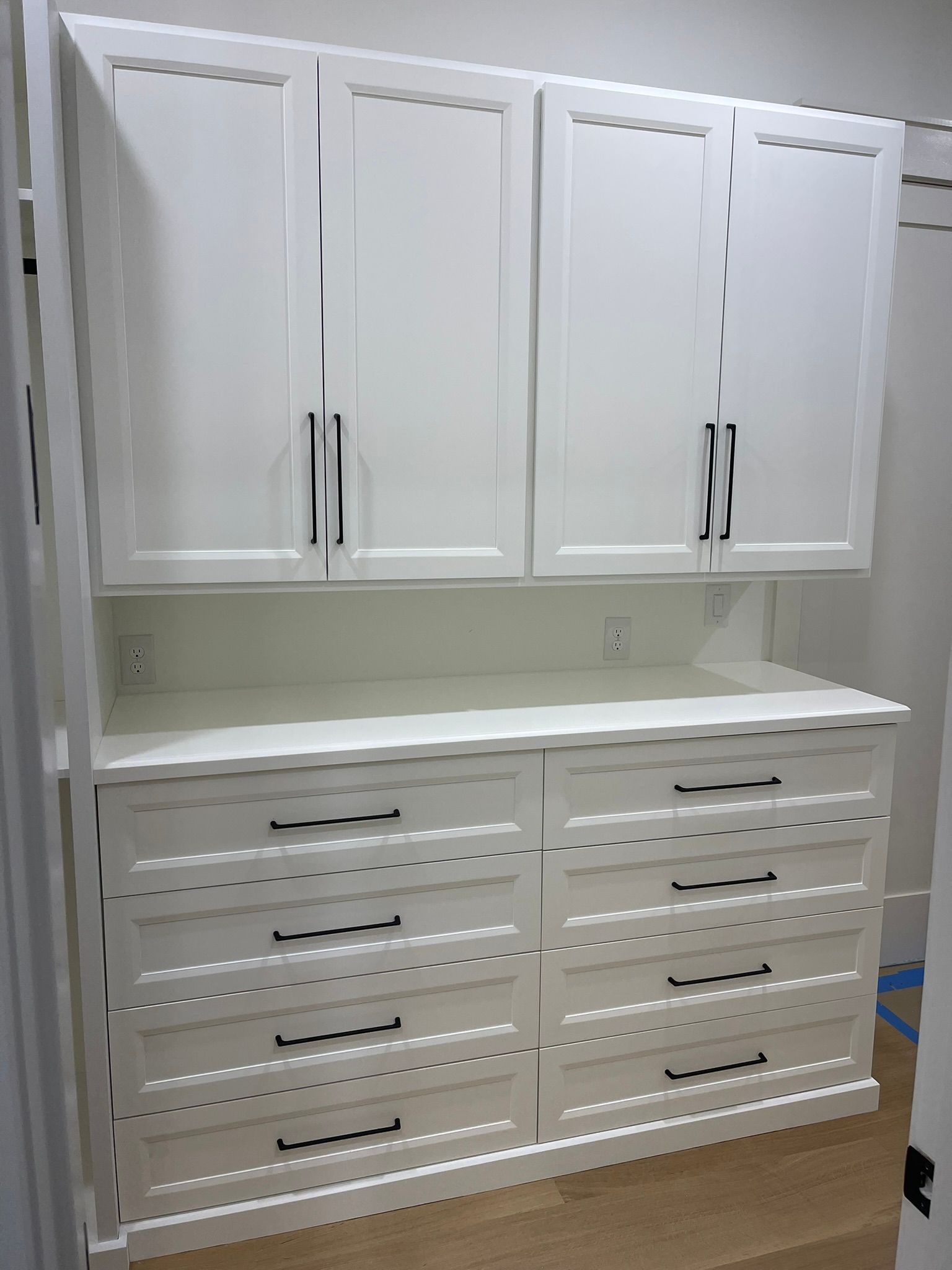 White built-in storage unit with upper cabinets and lower drawers. Black hardware on a white wall.