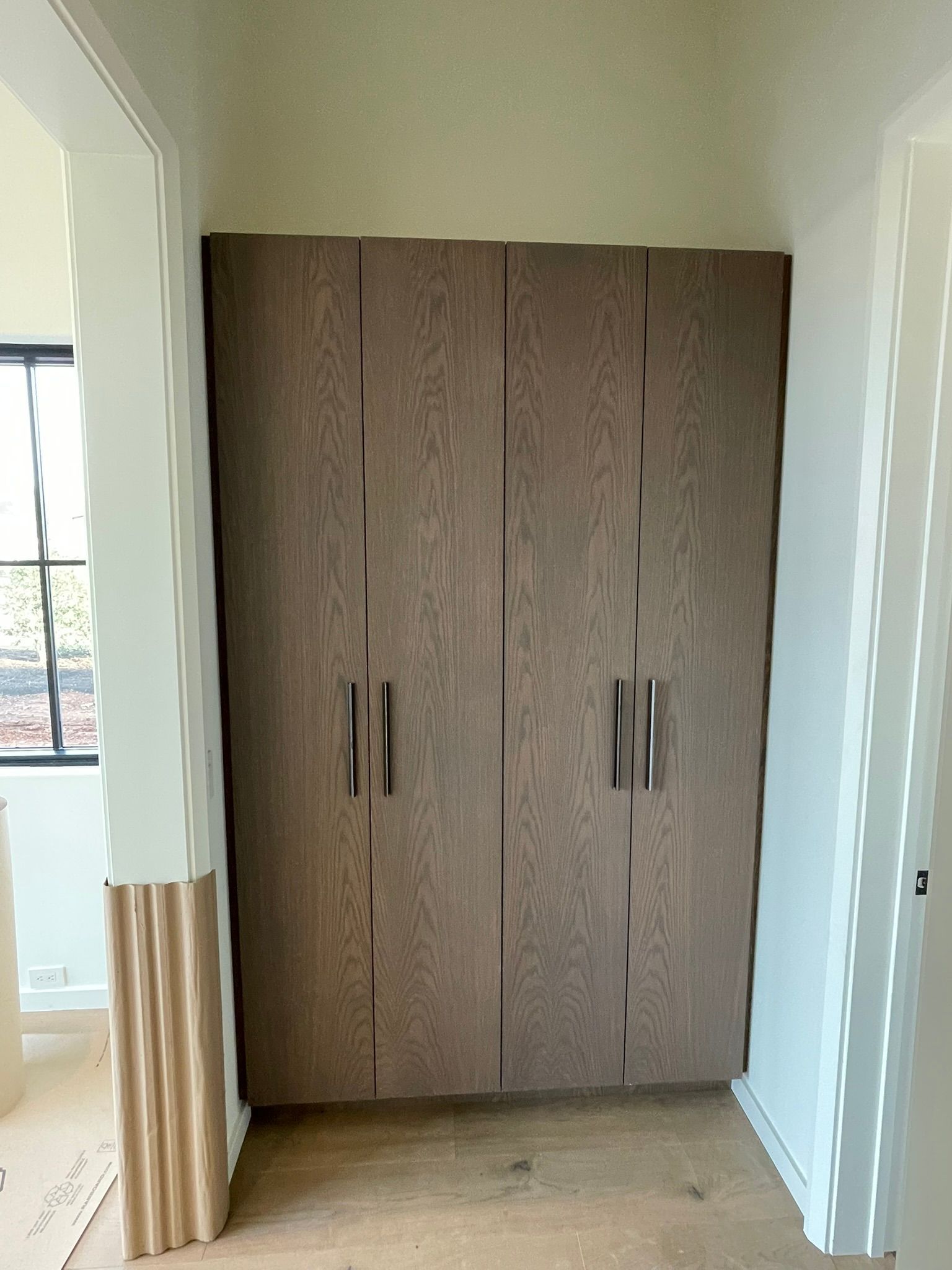 Built-in wood-grain wardrobe with dark handles in a room with white trim and a window.