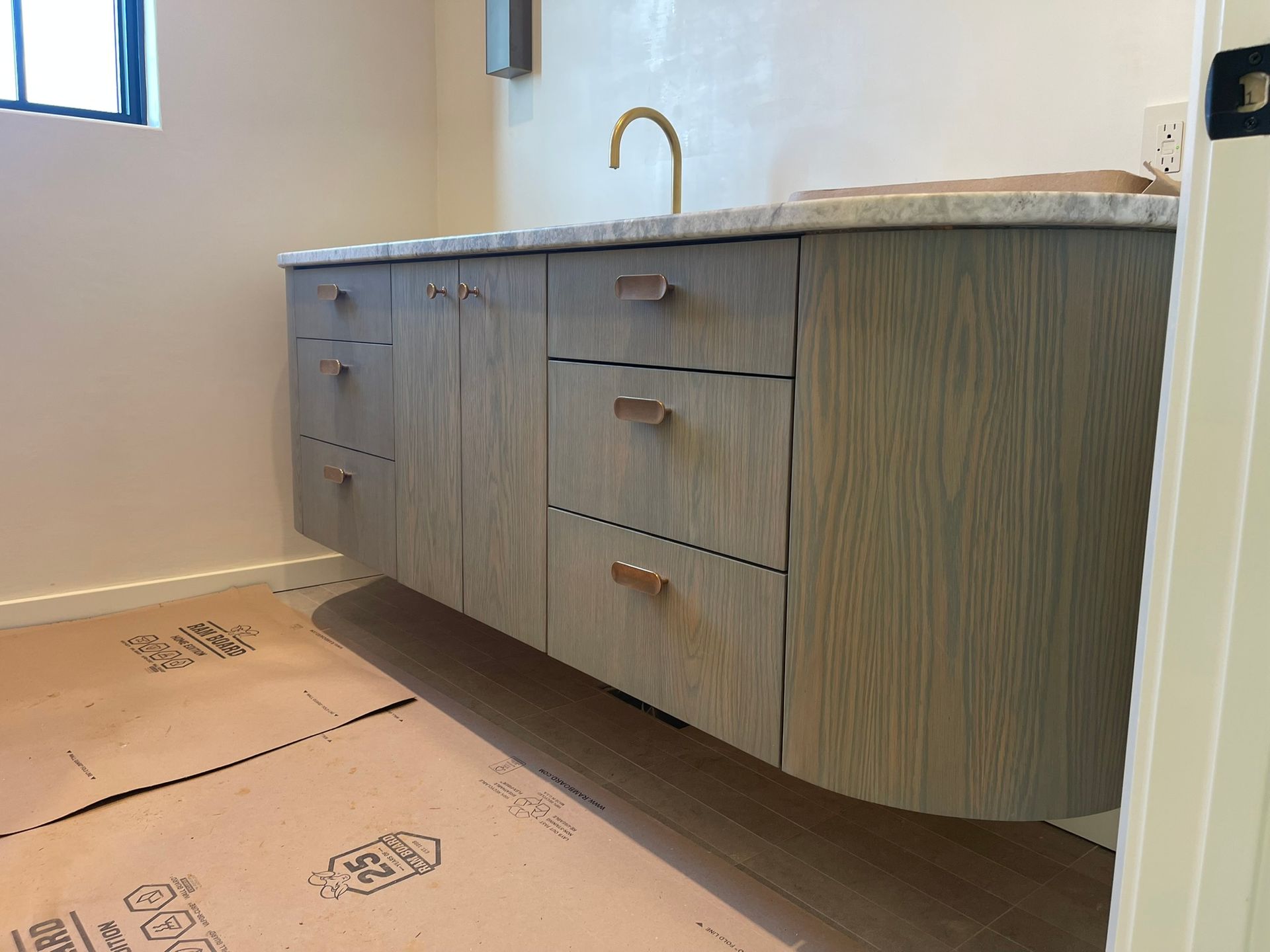 Floating gray wooden bathroom vanity with drawers, a marble countertop, and gold faucet.