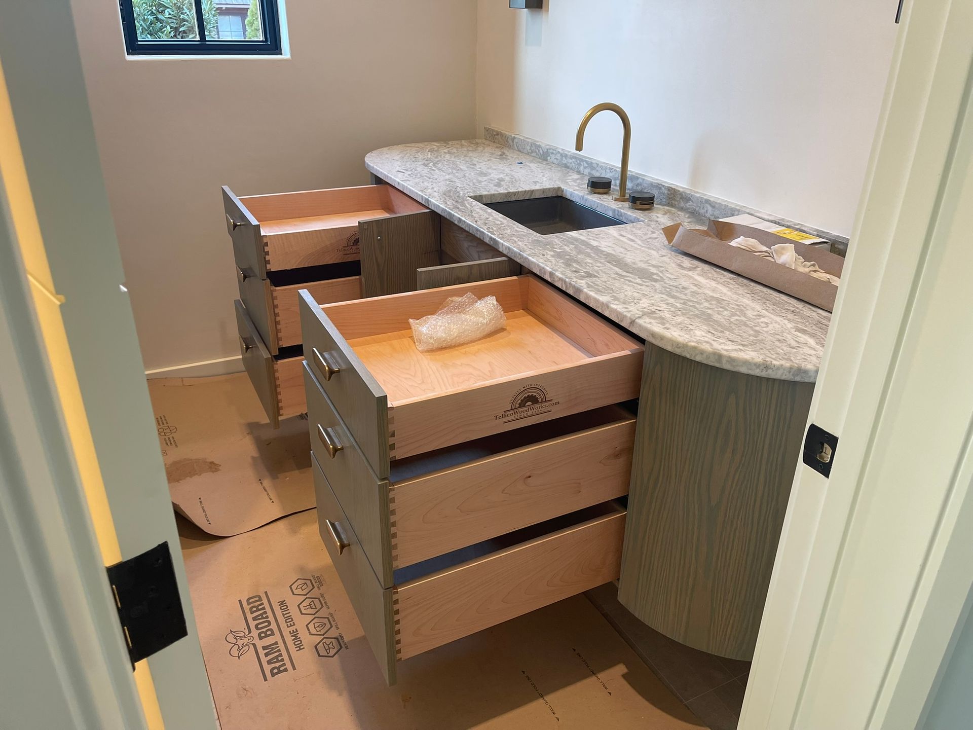 Bathroom vanity with open drawers, light wood and grey cabinets, granite countertop, gold faucet.