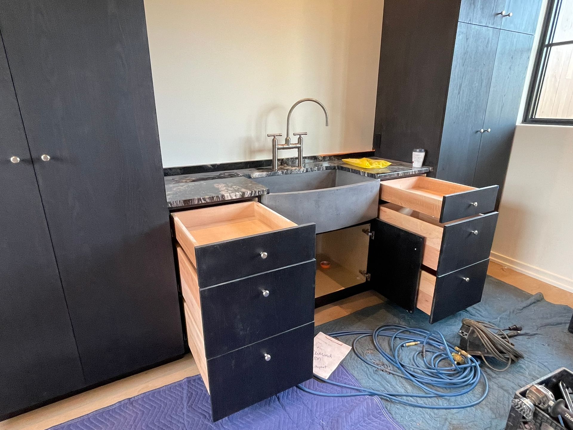 Black cabinets with open drawers under a sink, construction in progress.