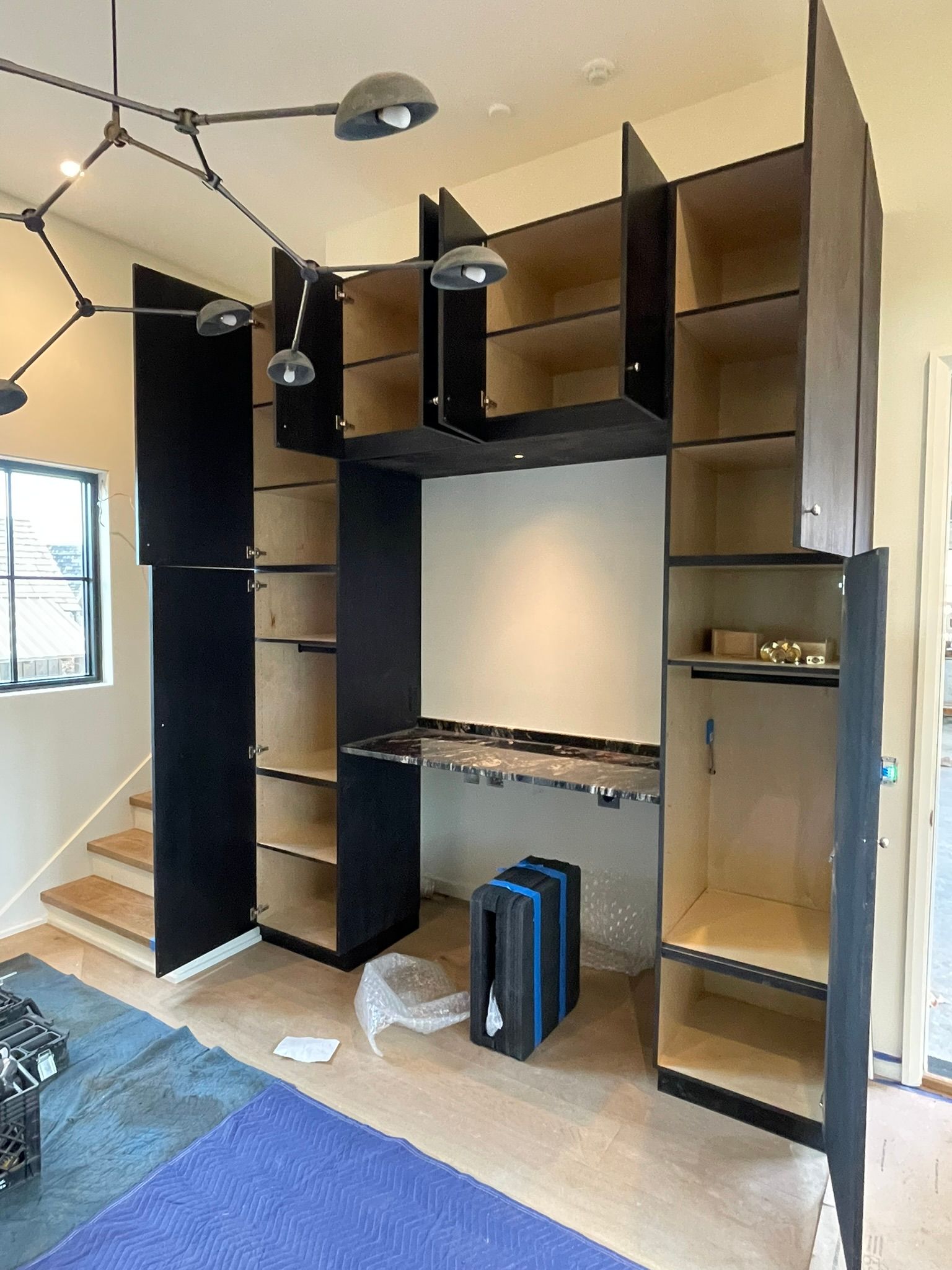 Black built-in shelves and desk under construction in a room with a staircase.