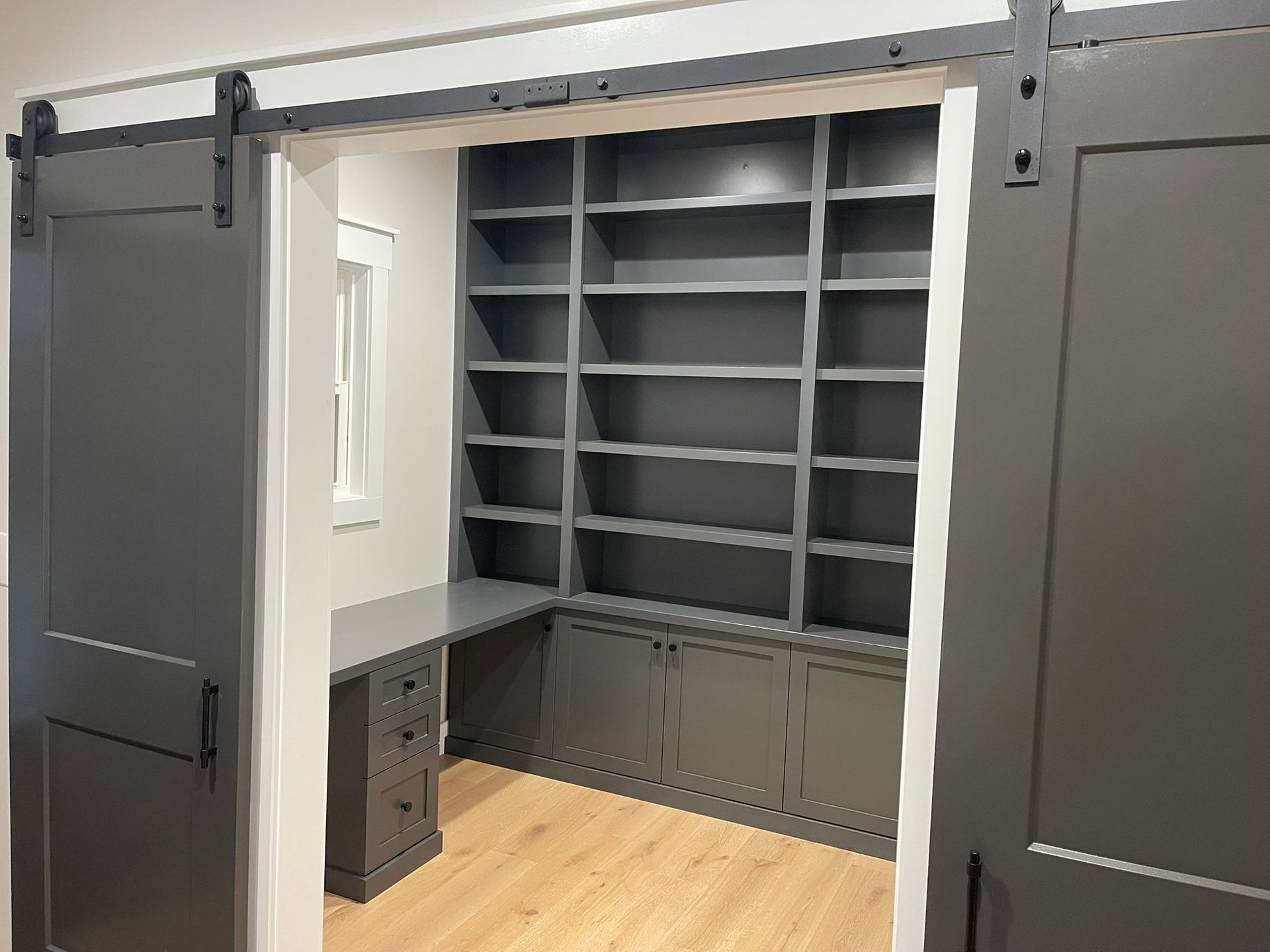 Gray built-in home office with bookshelves, desk, and sliding barn doors.