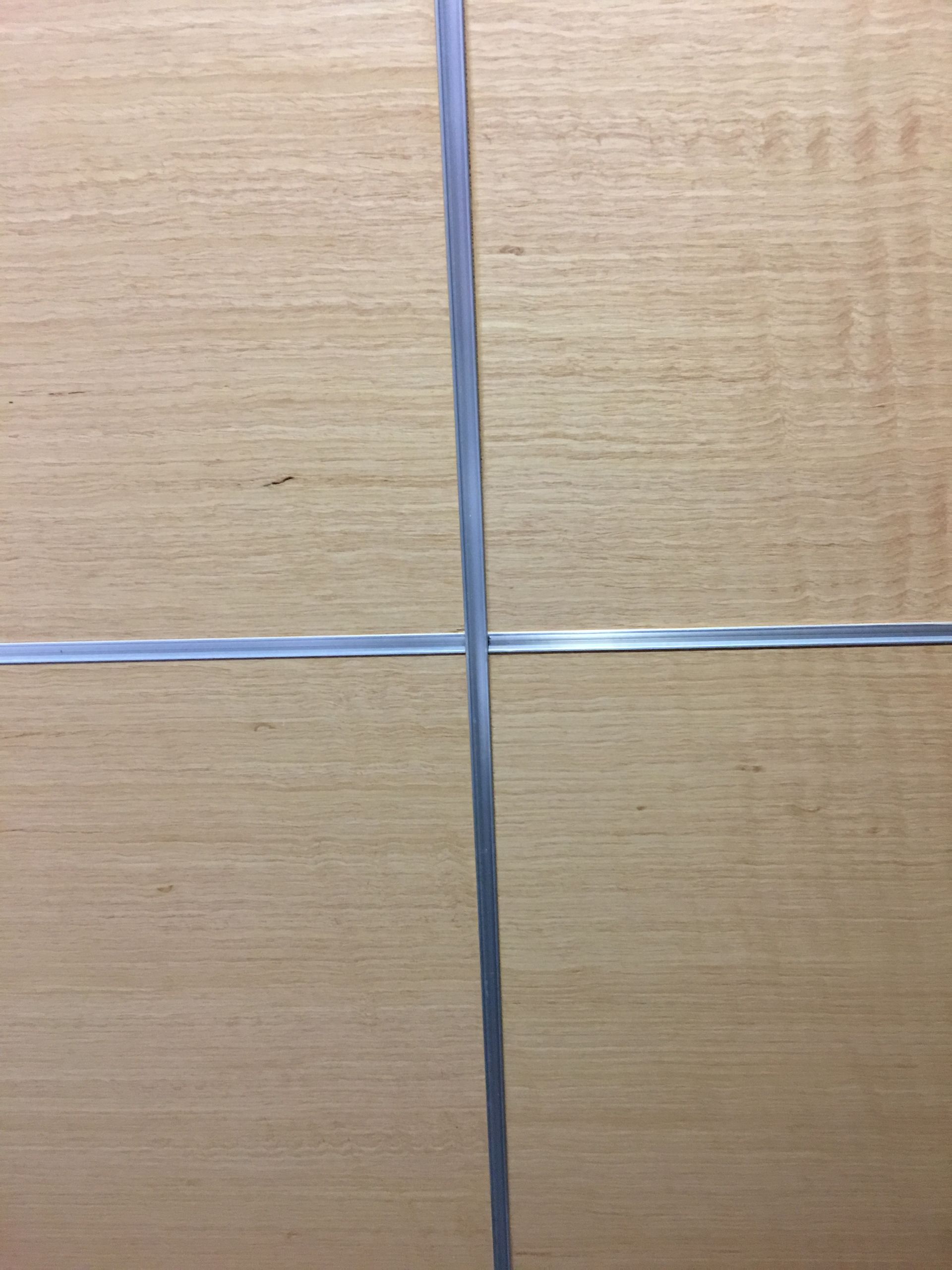 Tan wooden surface with a silver metallic stripe intersecting another, dividing it into four sections.