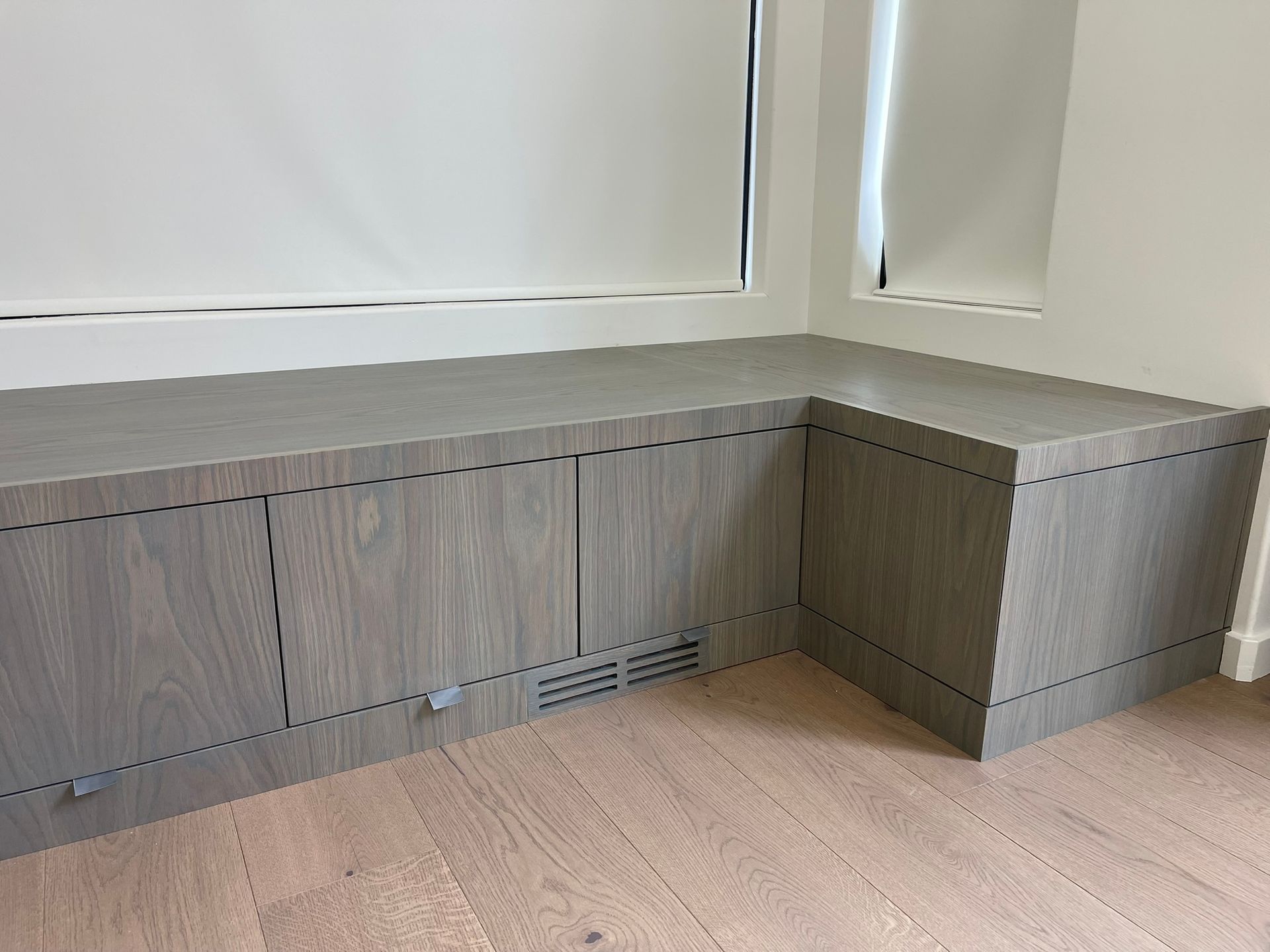 Gray wooden built-in storage bench under a window, with doors and a vent.