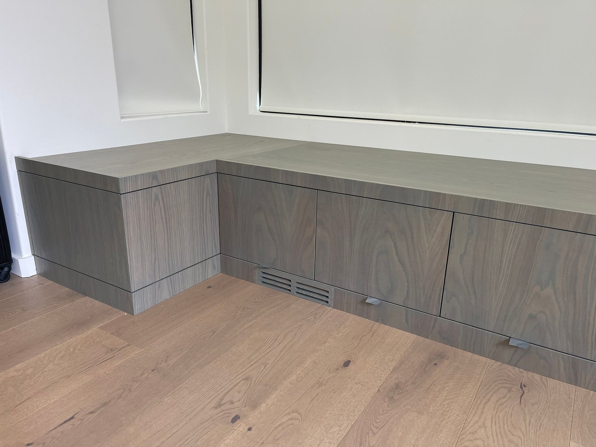 L-shaped gray wooden storage cabinet against a wall with a window and hardwood floor.