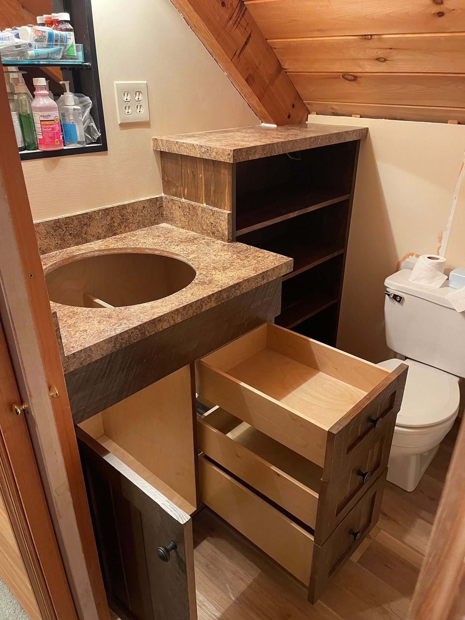 Bathroom with wooden vanity, open drawers, sink, granite countertop, and toilet.