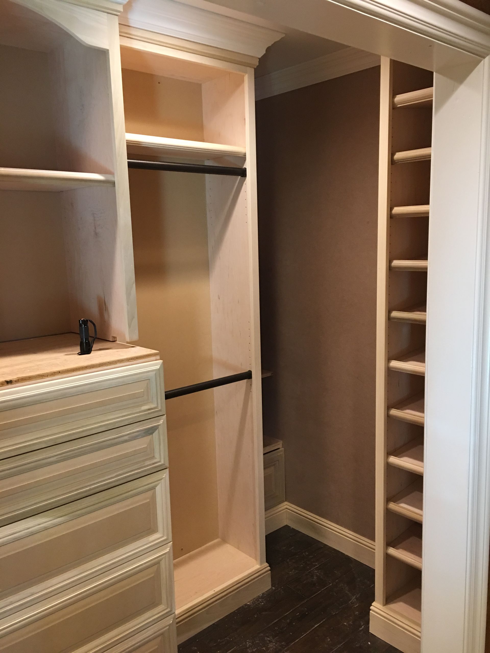 Empty built-in closet with shelves, drawers, and shoe storage. Beige color, dark flooring, and a brown wall.