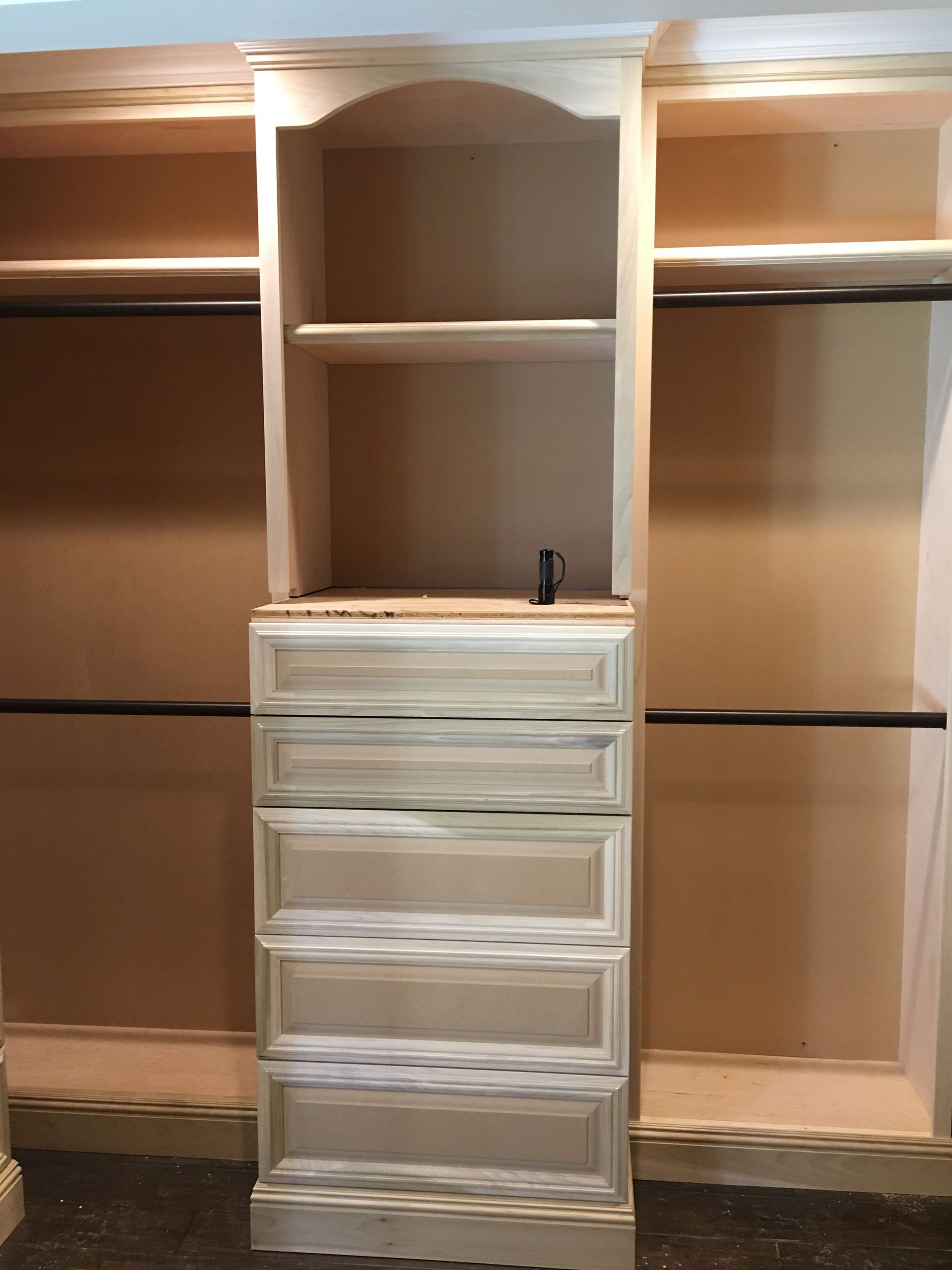 Built-in closet organizer with a central cabinet featuring shelves and drawers, flanked by hanging rods.