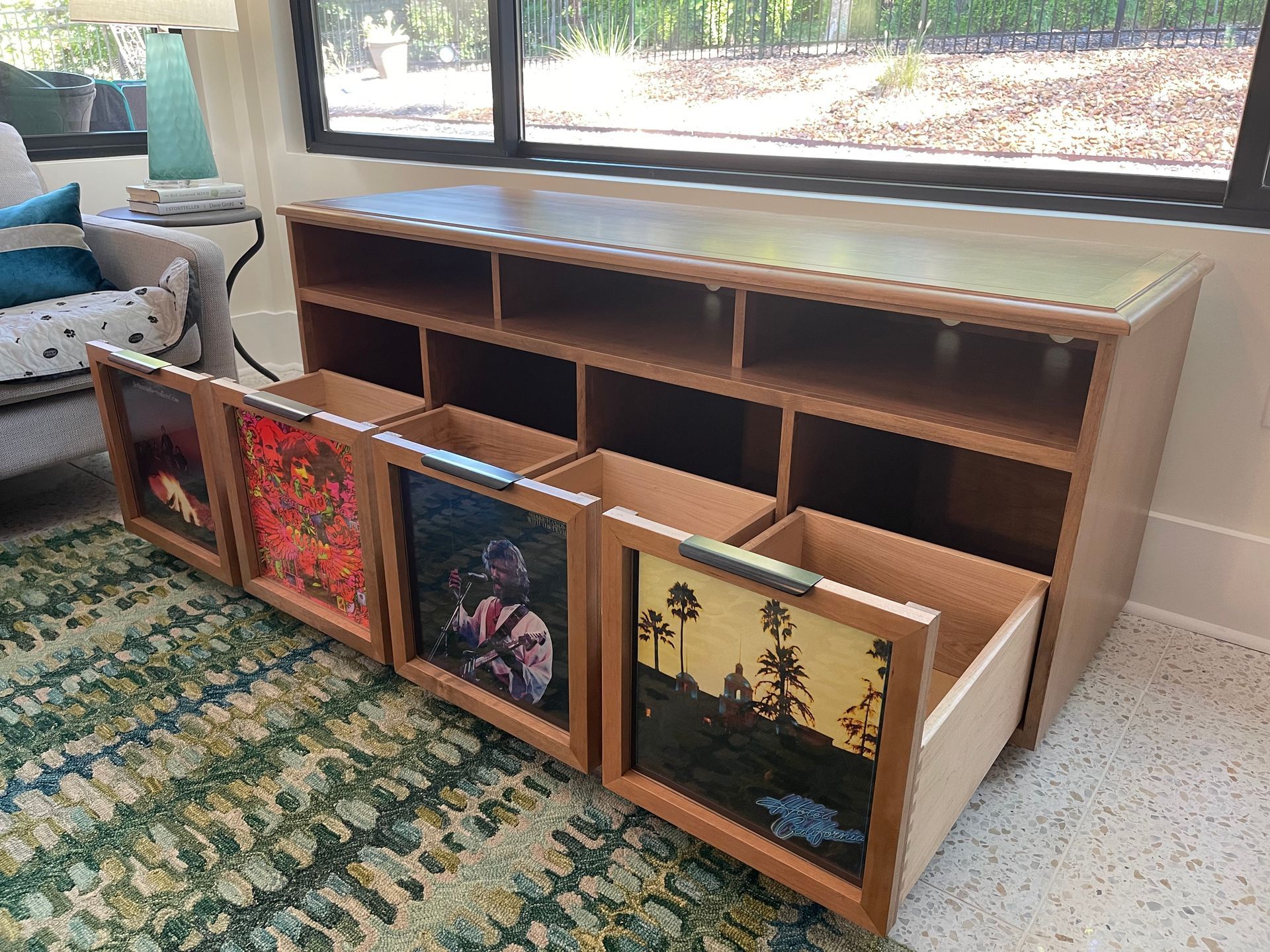 Wooden cabinet with open drawers displaying album covers, in front of a window.