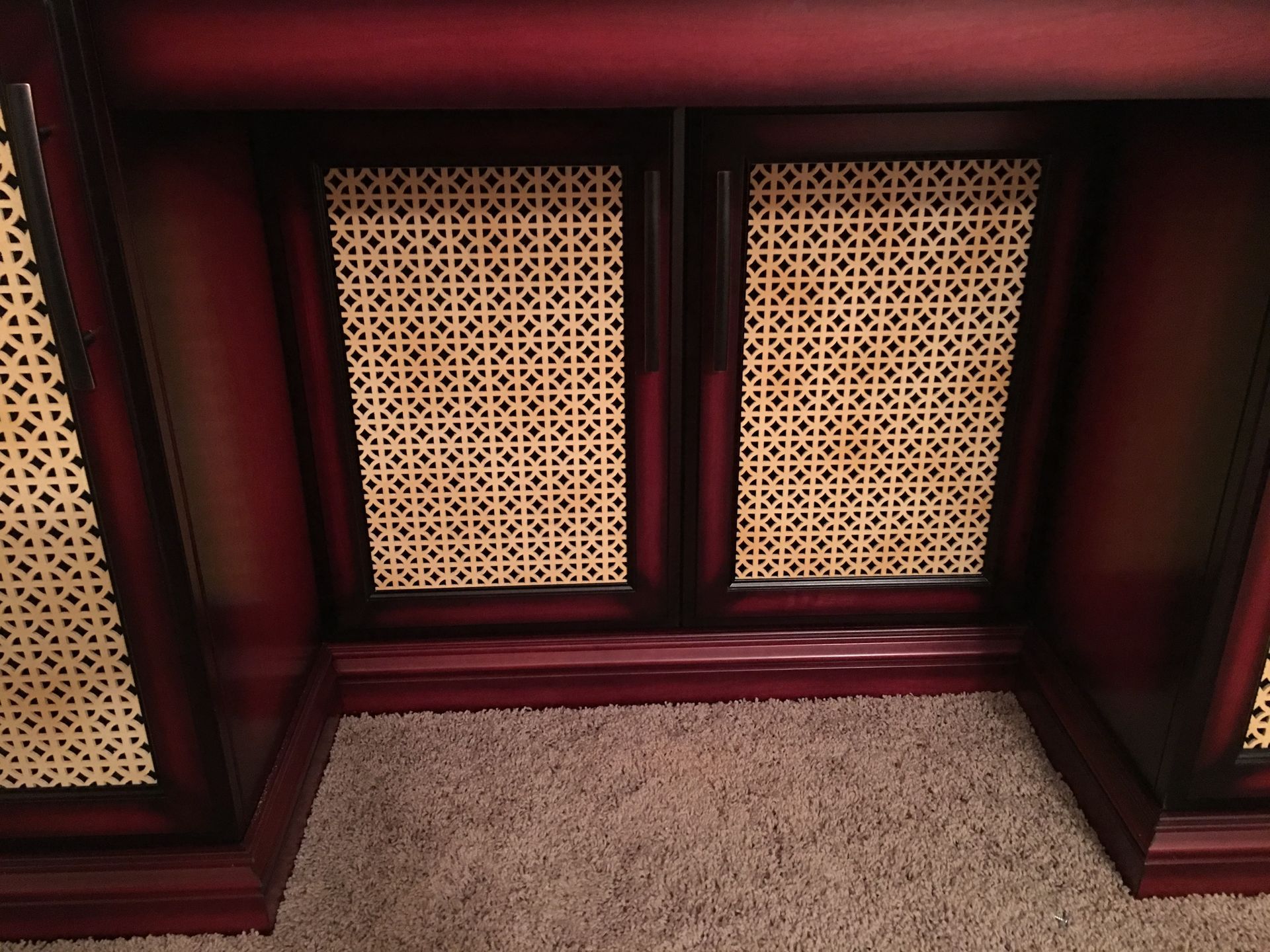 Dark wooden cabinet with woven panels on doors, set on carpet.