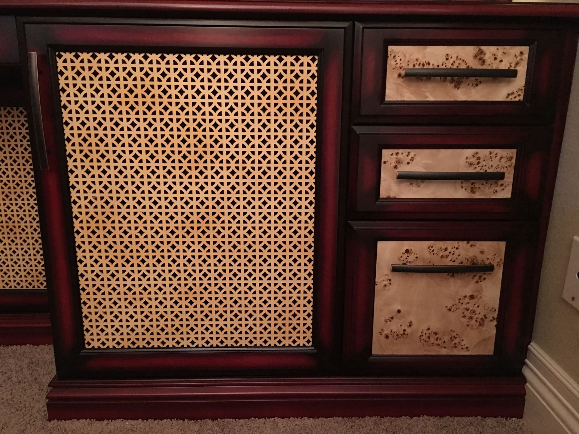Dark red cabinet with woven panel door and three drawers, with antique-style handles.