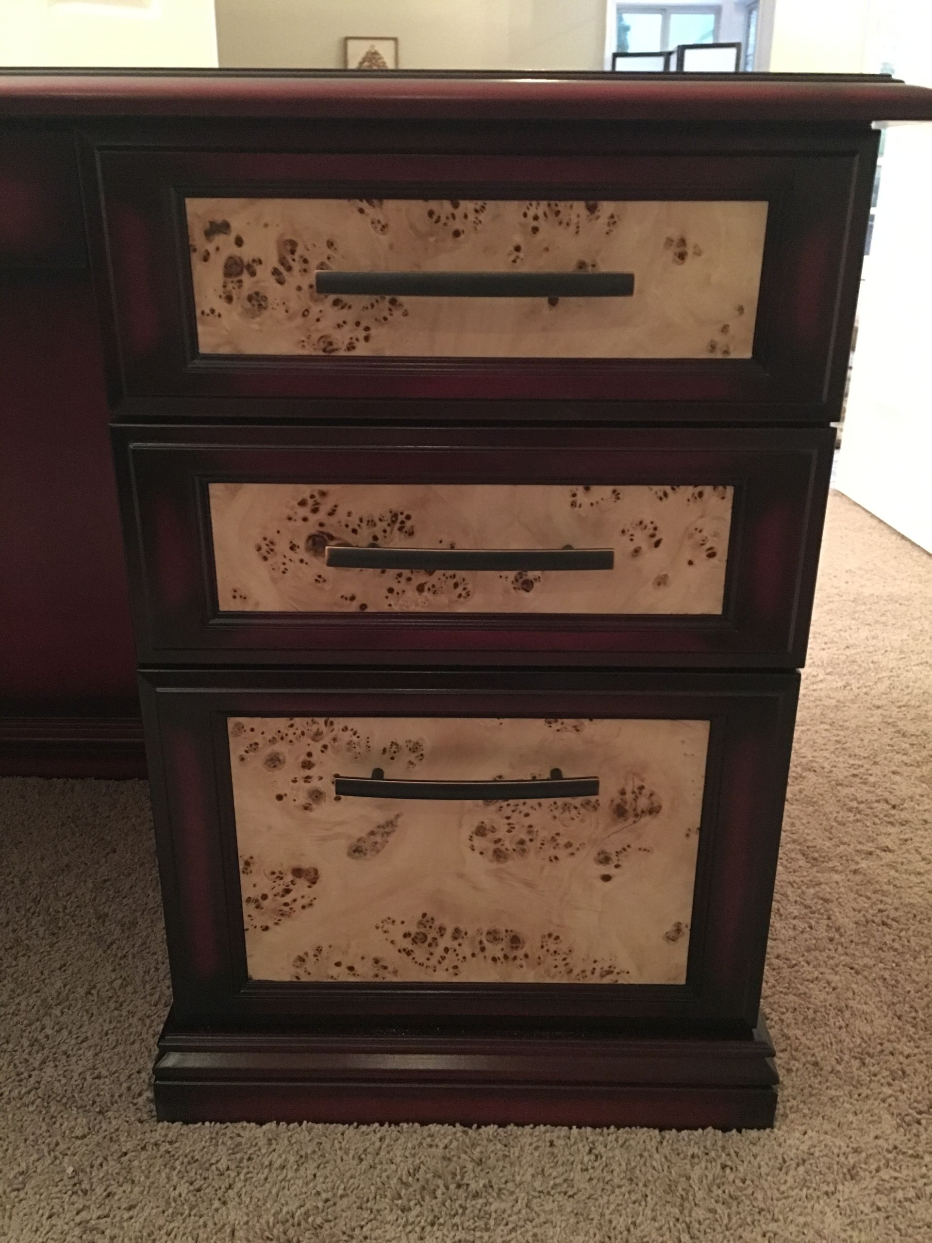 Three-drawer desk cabinet with reddish-brown wood frame and light-colored, patterned drawer fronts.