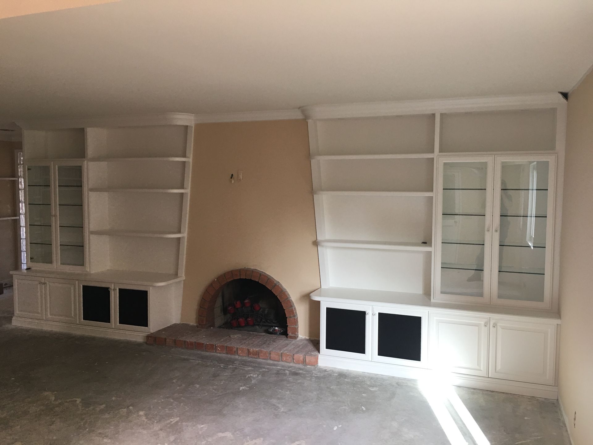 Built-in white bookshelves flanking a fireplace, with glass-doored cabinets and black lower panels.