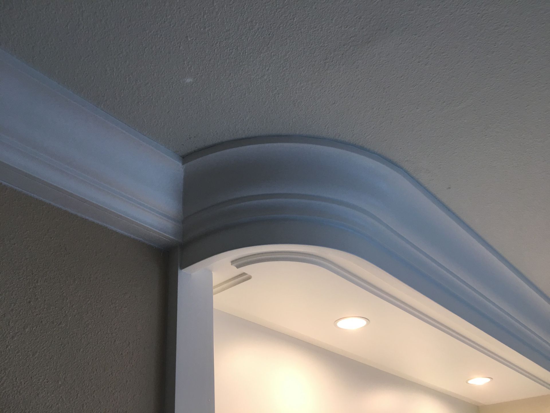 White curved molding at the corner of a doorway, against beige wall and textured ceiling.