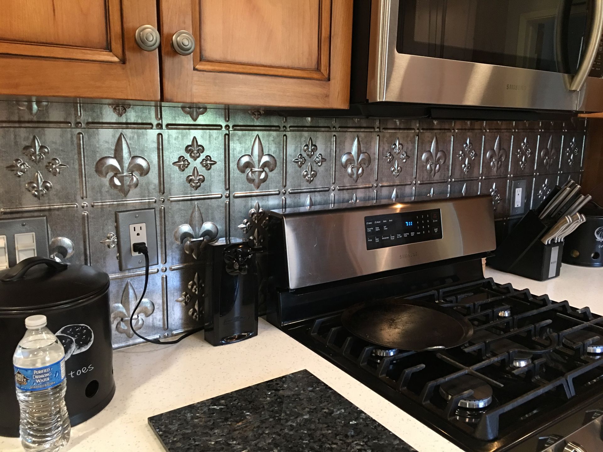 Kitchen backsplash with fleur-de-lis tiles above a stove. Cabinets are wooden.