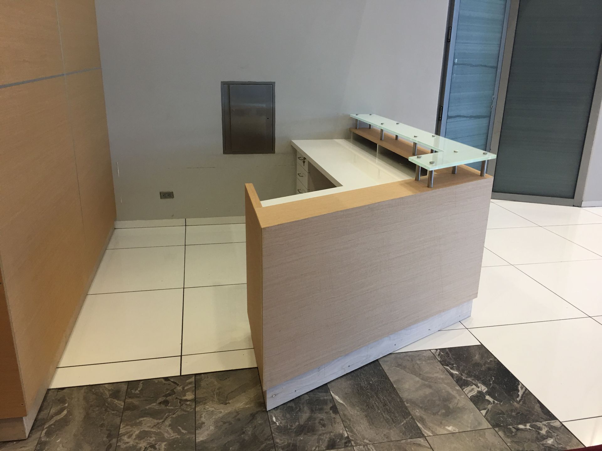 Beige and white office reception desk in a modern building with tile flooring.