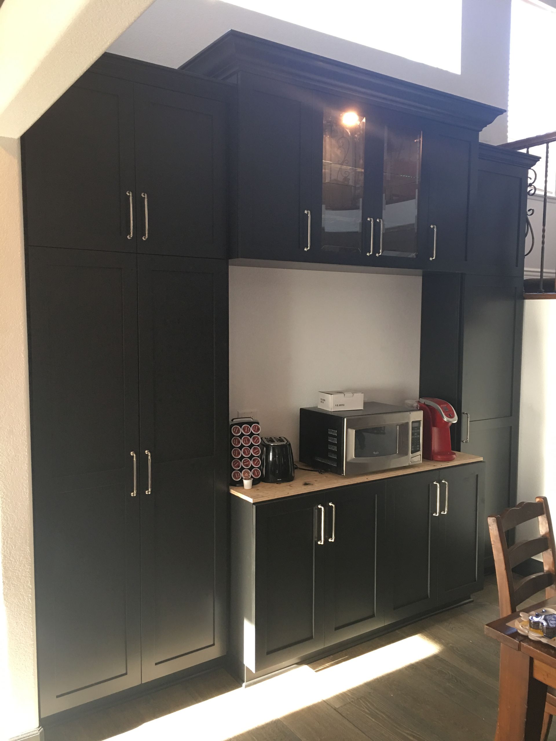 Black cabinetry in a kitchen, including tall storage, lower cabinets, and a microwave.