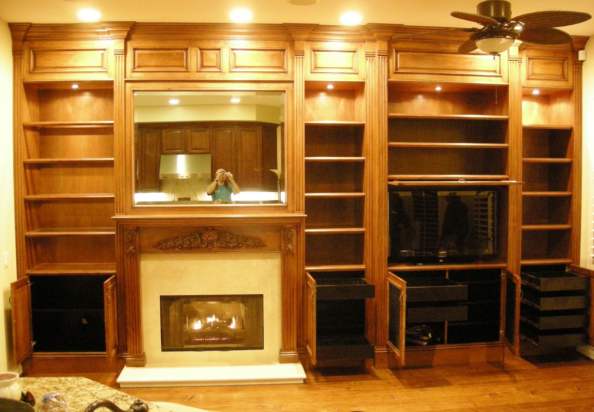 Wooden built-in shelving and cabinets surround a fireplace and TV. Recessed lighting.