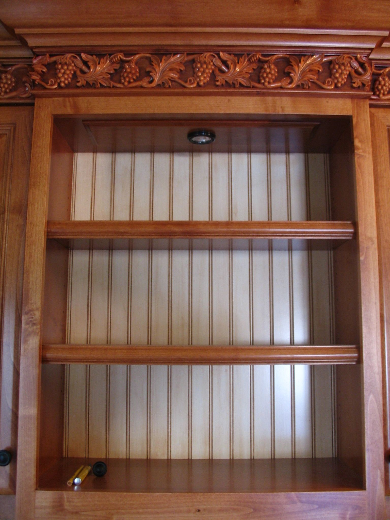 Wooden cabinet with shelves, decorative carving, and vertical fabric back panel.
