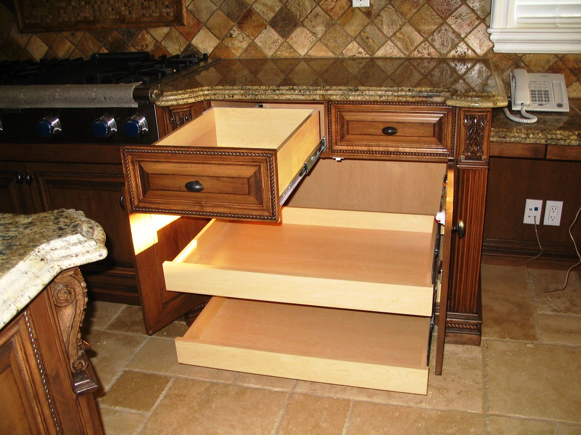 Wooden kitchen cabinet with drawers and pull-out shelves; granite countertop.