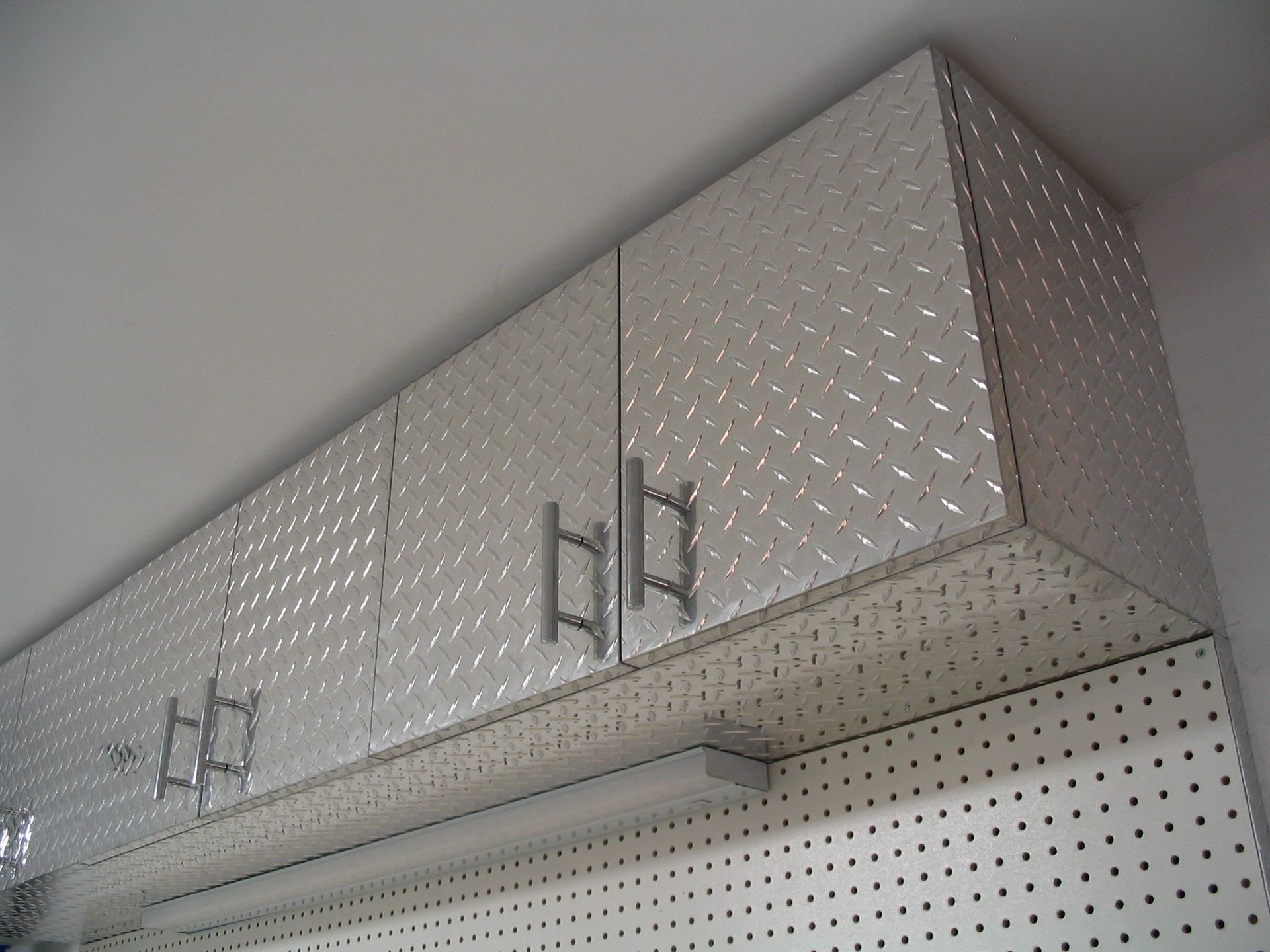 Overhead metal storage cabinets in a garage, mounted above a pegboard wall.