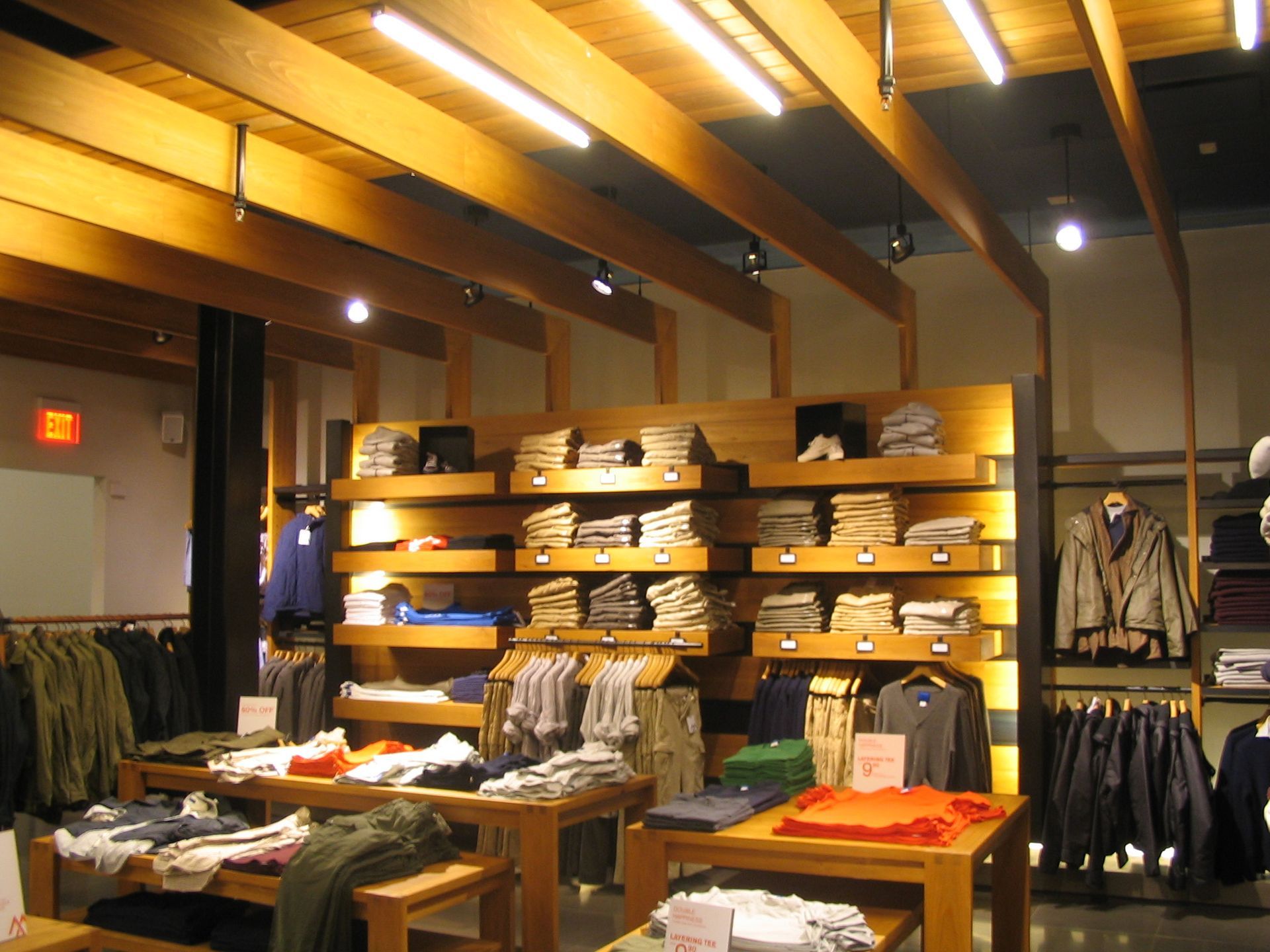 Clothing store interior with wooden shelving displaying folded shirts and tables displaying clothes.