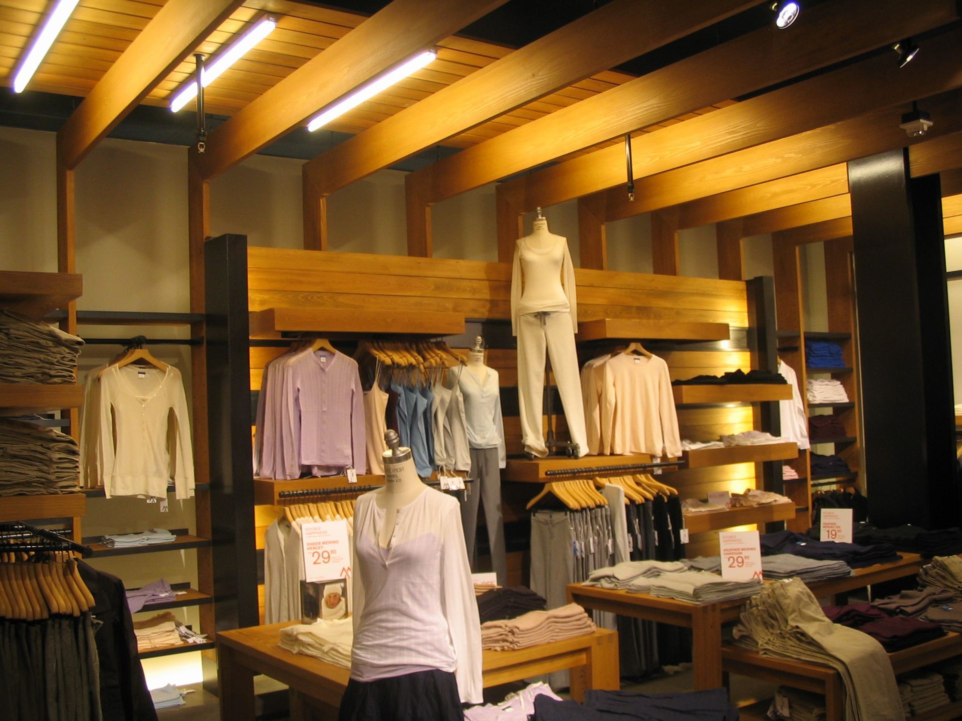 Clothing store interior with clothing displays, wooden beams, and mannequins.