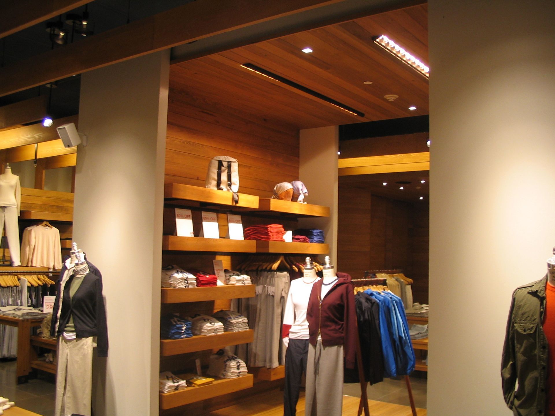 Clothing store interior with wooden shelves displaying shirts and sweaters. Mannequins model outfits.