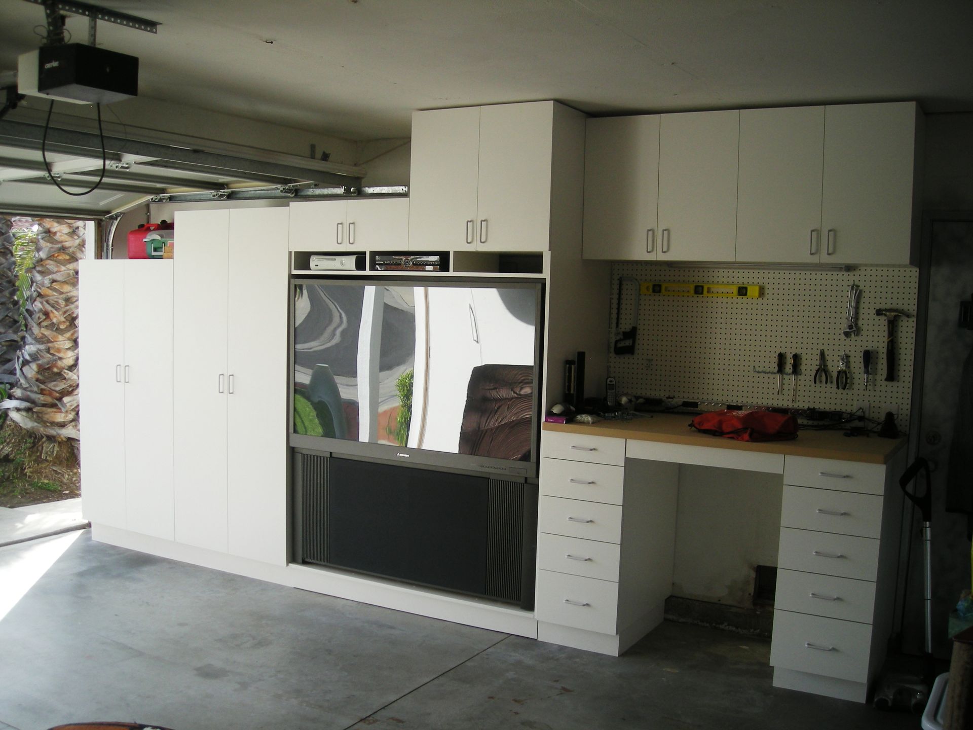 Garage interior with white cabinets, a workbench, and a pegboard tool organization system.
