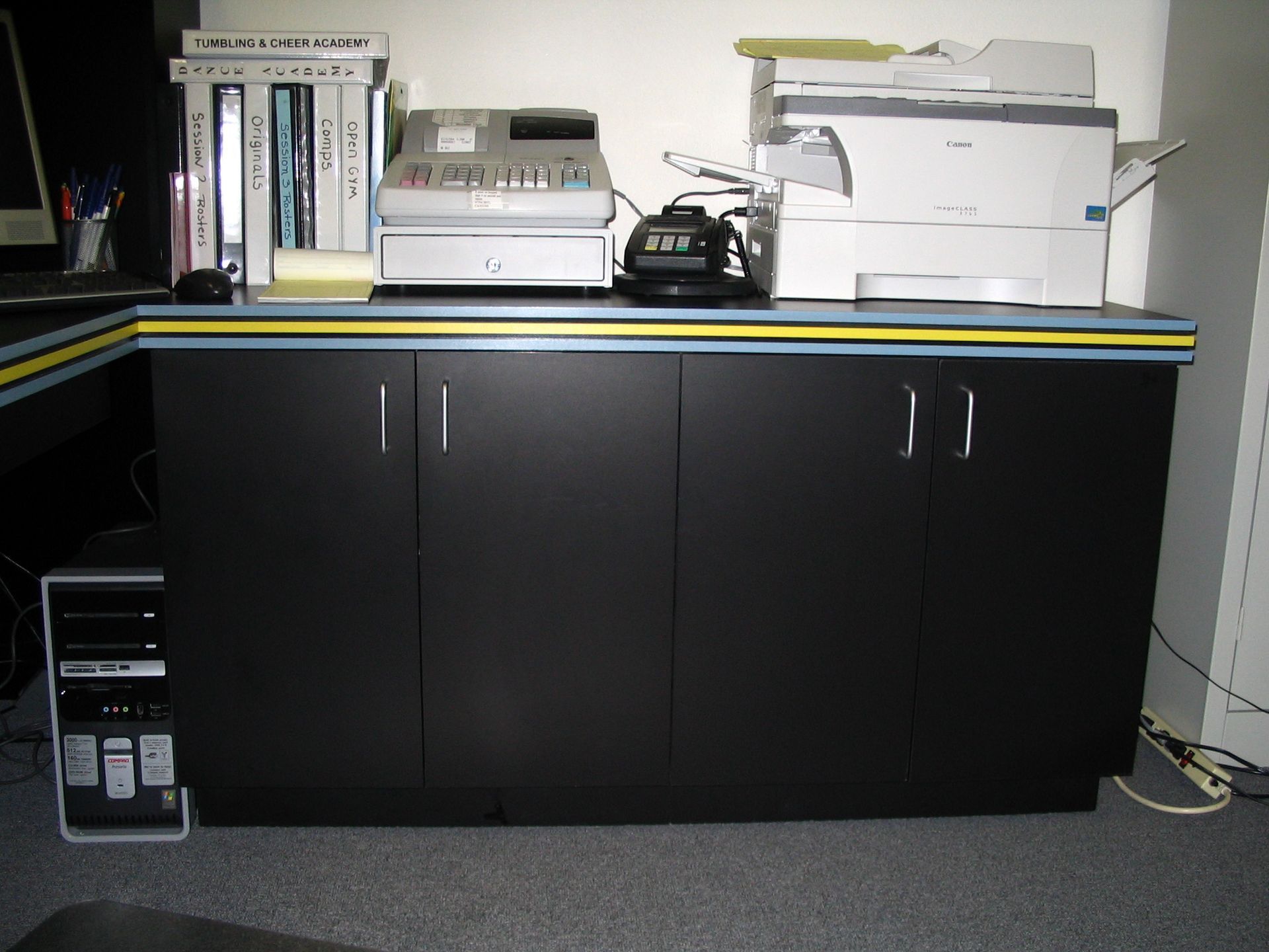 Black cabinet with printer, cash register, and phone on top, computer next to it.