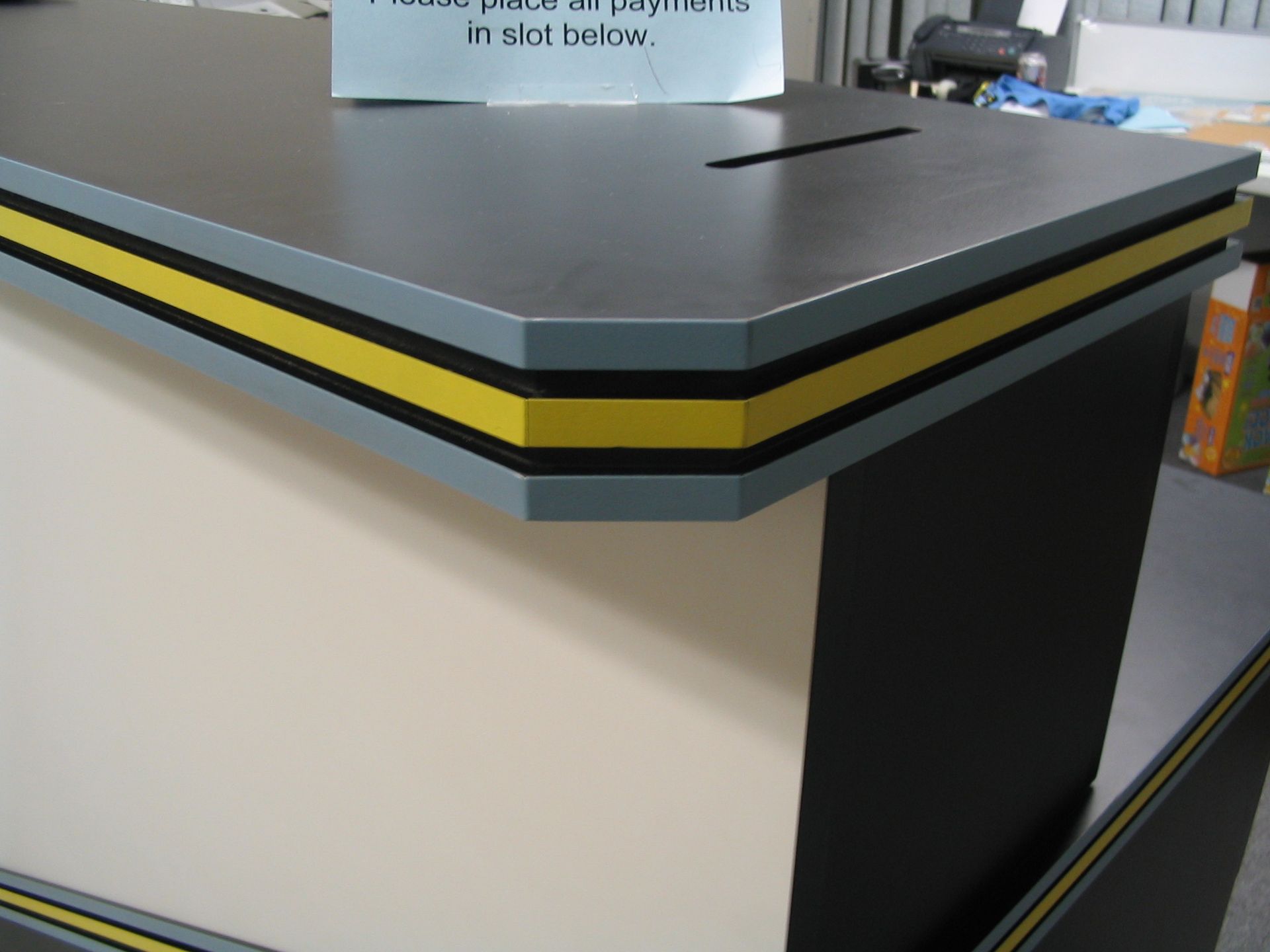 Close-up of a desk with a slot for payments. Gray, black, and yellow accents.