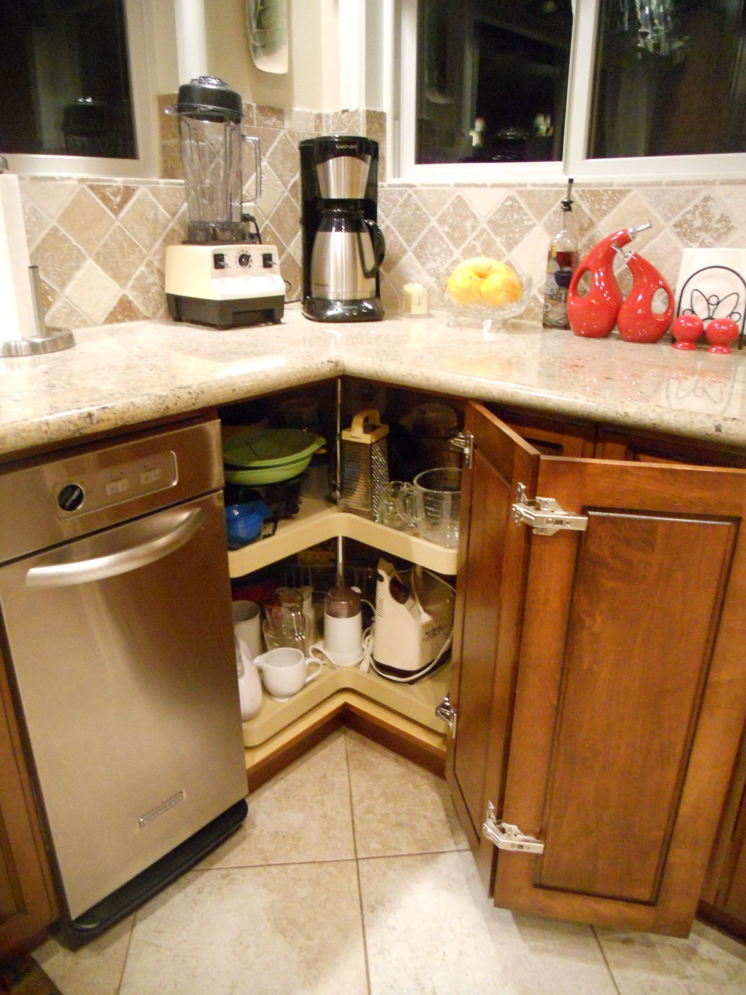 Corner kitchen cabinet with open door revealing spinning shelves with stored items. Stainless steel dishwasher visible.