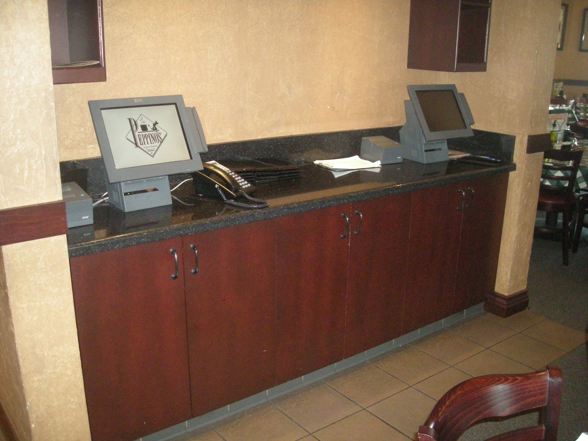 Restaurant counter with two point-of-sale systems on a dark countertop above dark wood cabinets.
