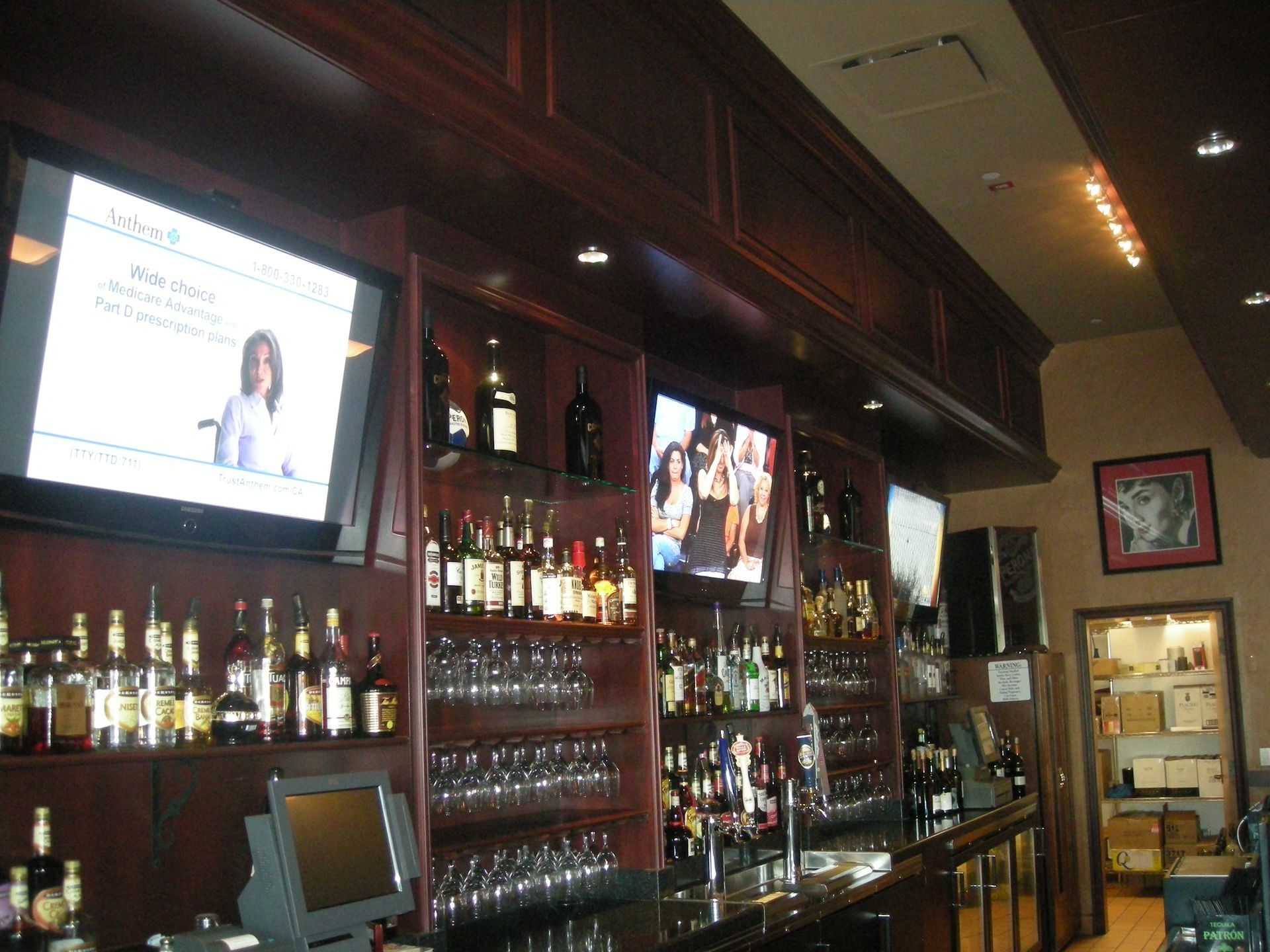 Bar interior with liquor bottles, glassware, and multiple TVs, all set against dark wood.