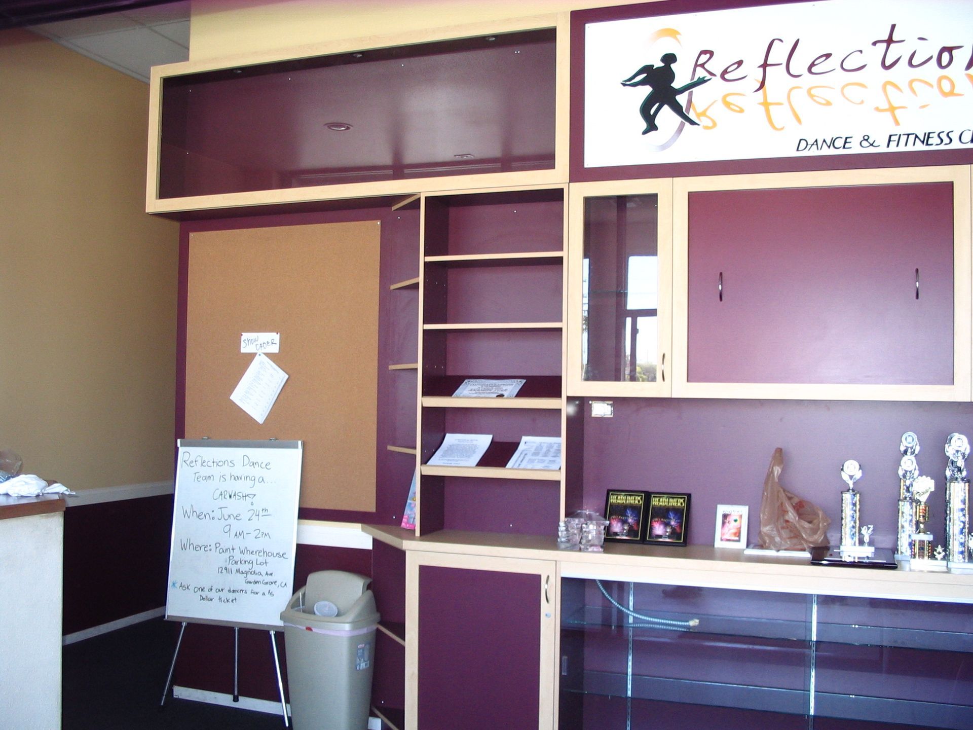Interior of a business with maroon and beige cabinets, shelves, a bulletin board, and trophies.
