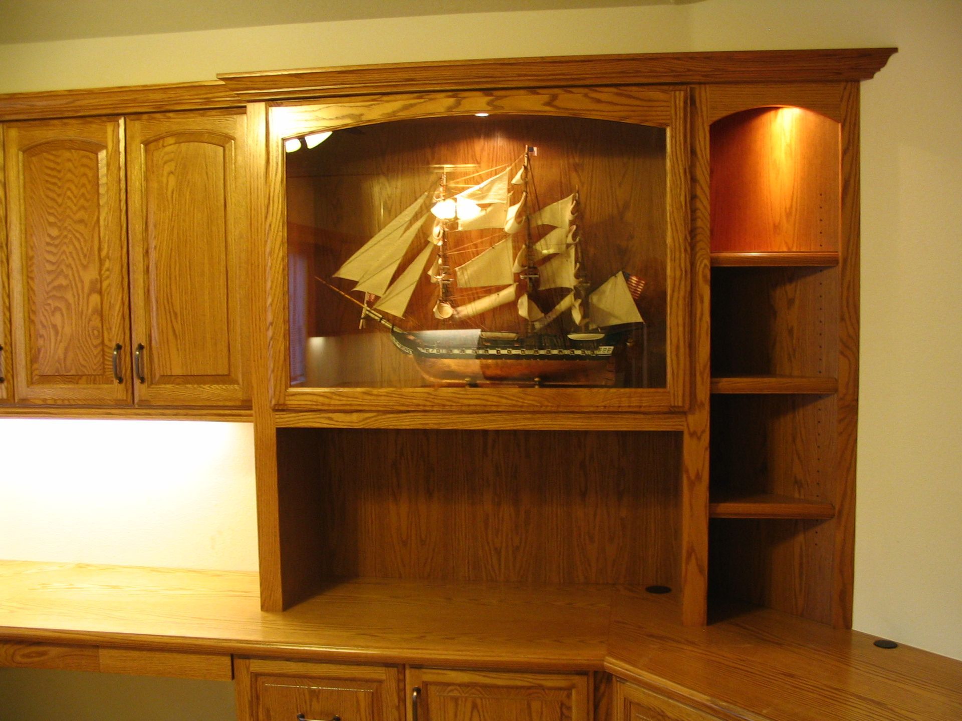 Built-in oak cabinet with illuminated ship model in glass case, and shelves.