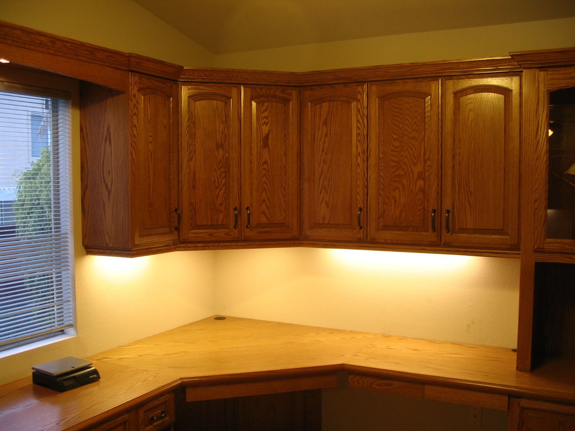 Wooden desk and cabinets with under-cabinet lighting near a window.
