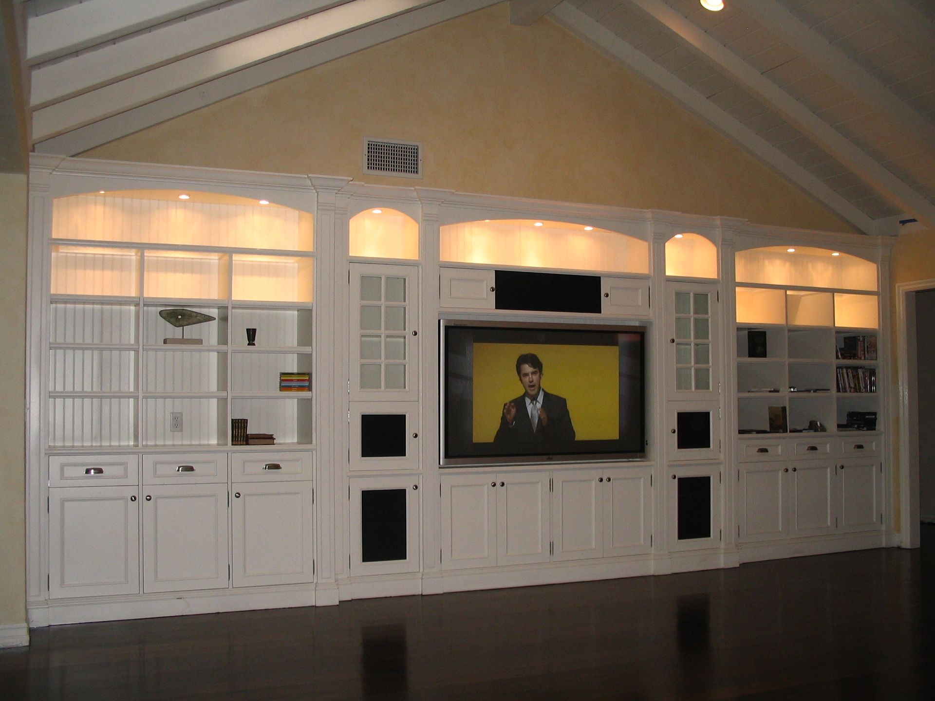 White built-in entertainment center with television, bookshelves, and cabinet storage. Interior of a home.